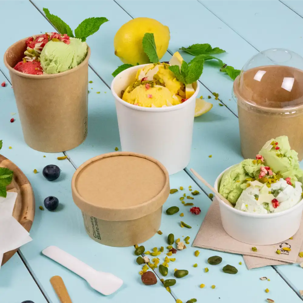 Two ice cream cups with different flavors, surrounded by mint leaves, fruit, and toppings on a blue table.
