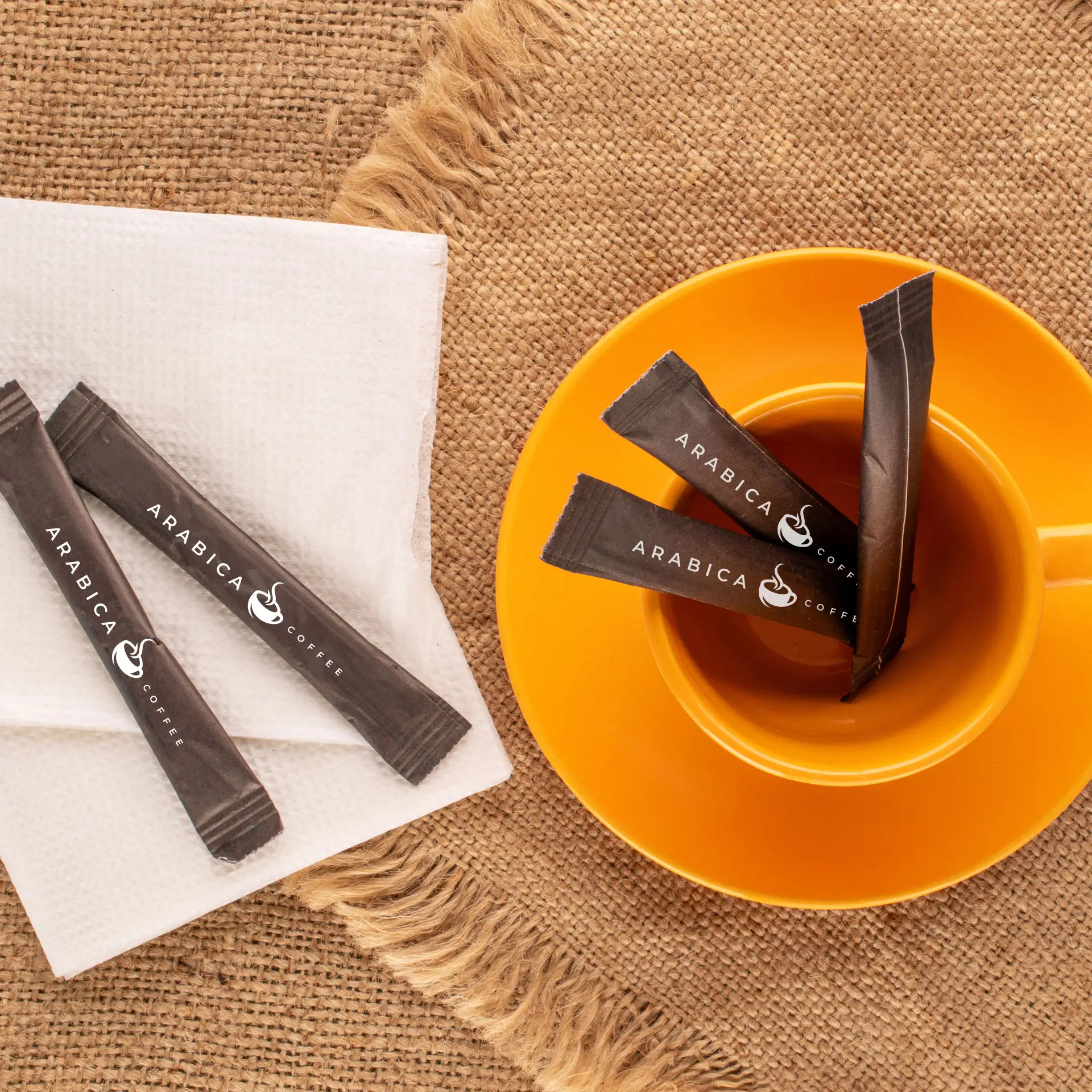 Brown organic cane sugar sticks displayed in an orange cup, with several sticks placed on a napkin and burlap backdrop.