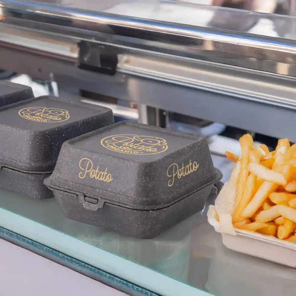 Two black burger boxes with gold "Potato" text and a serving of French fries on a glass surface.
