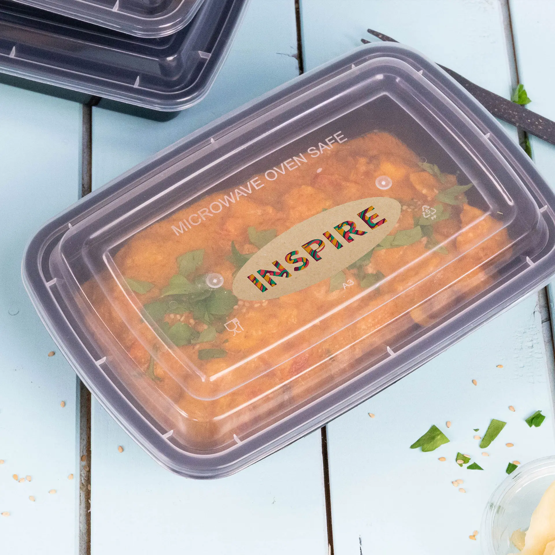 Microwave-safe container with food, featuring a clear lid and printed "INPSPIRE" label, on a light blue surface.