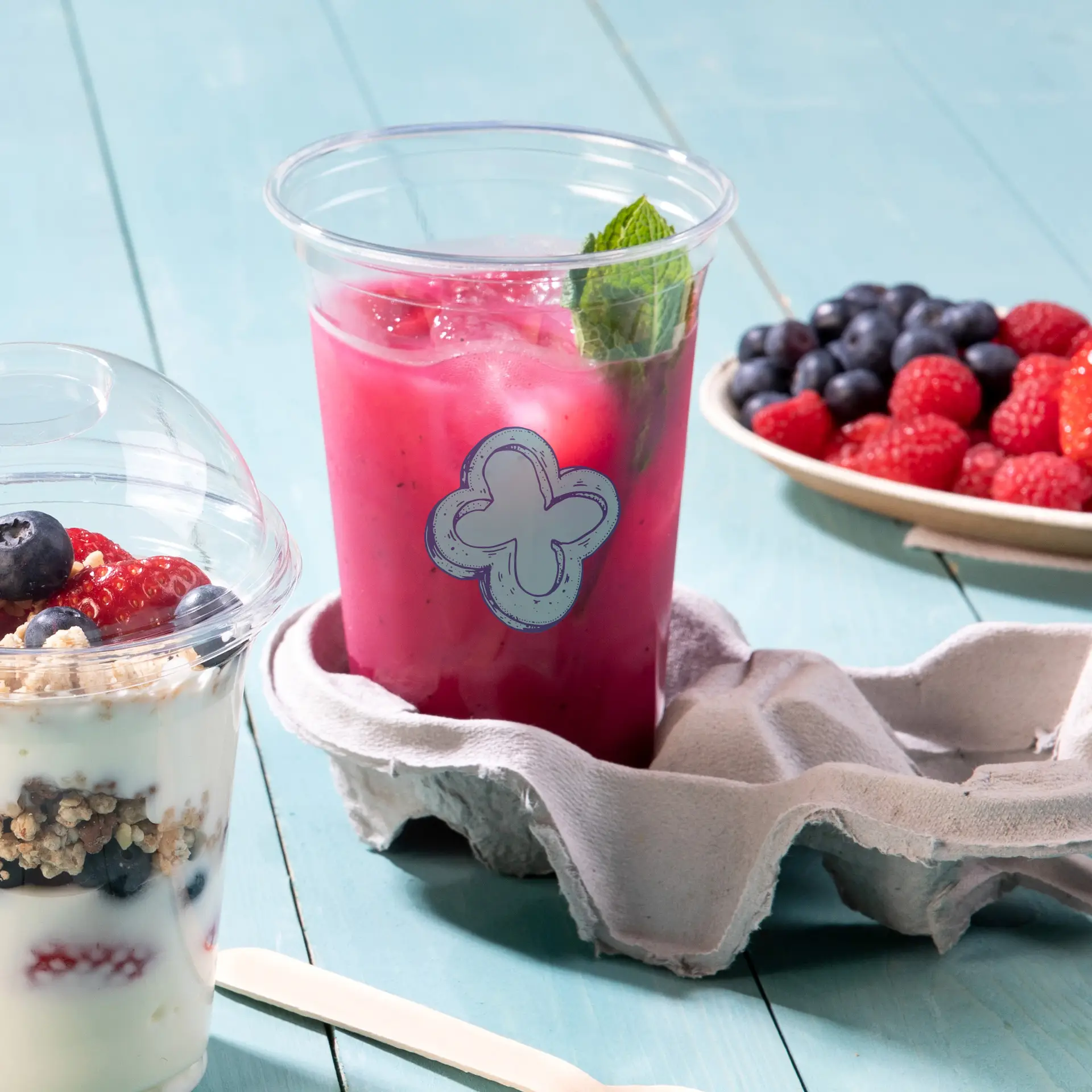 Clear 20 oz rPET cup with a decorative blue label, filled with a pink drink and garnished with mint, on a cloth backing.