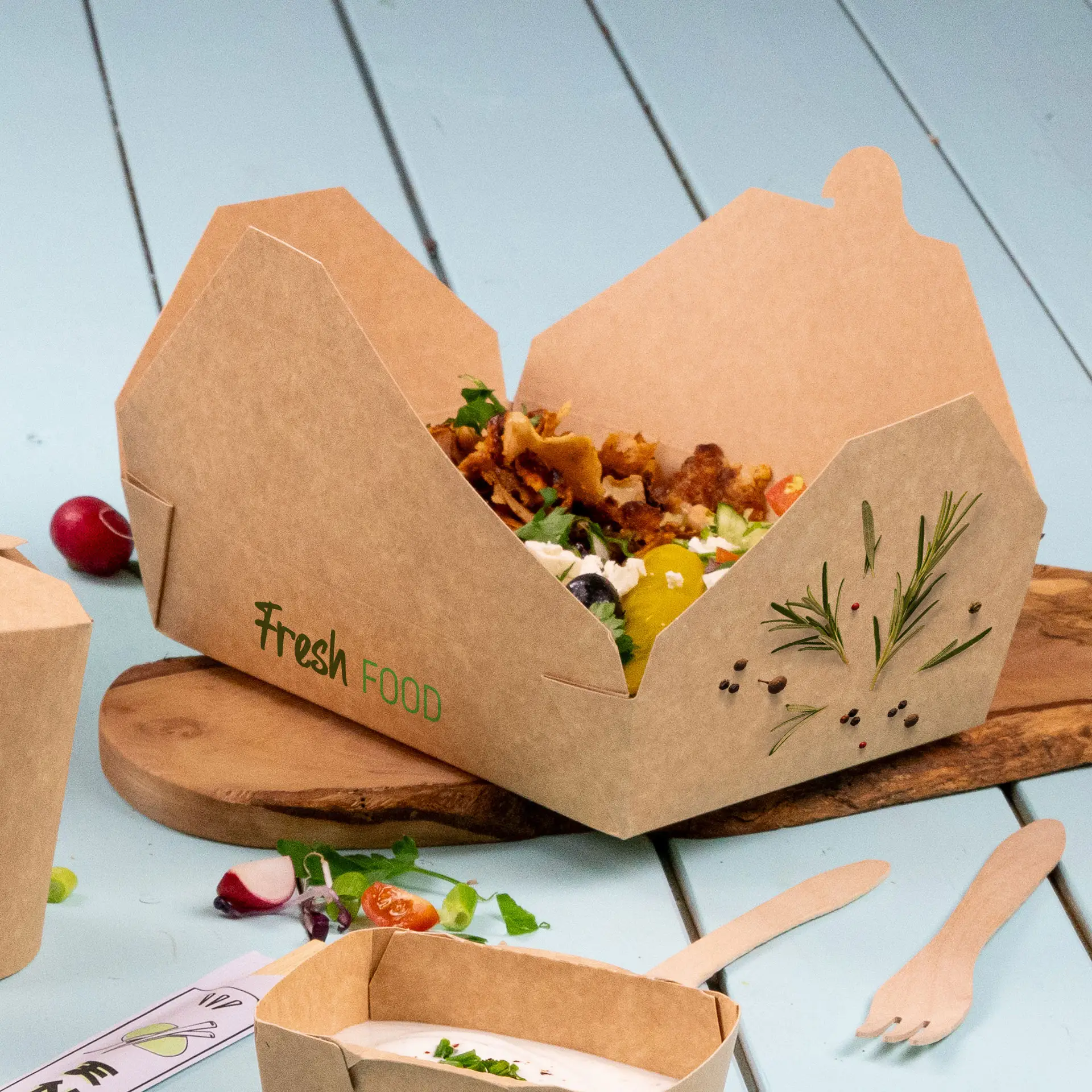 A takeaway box with a cardboard texture and "Fresh Food" printed, filled with a salad and garnished, on a wooden board.