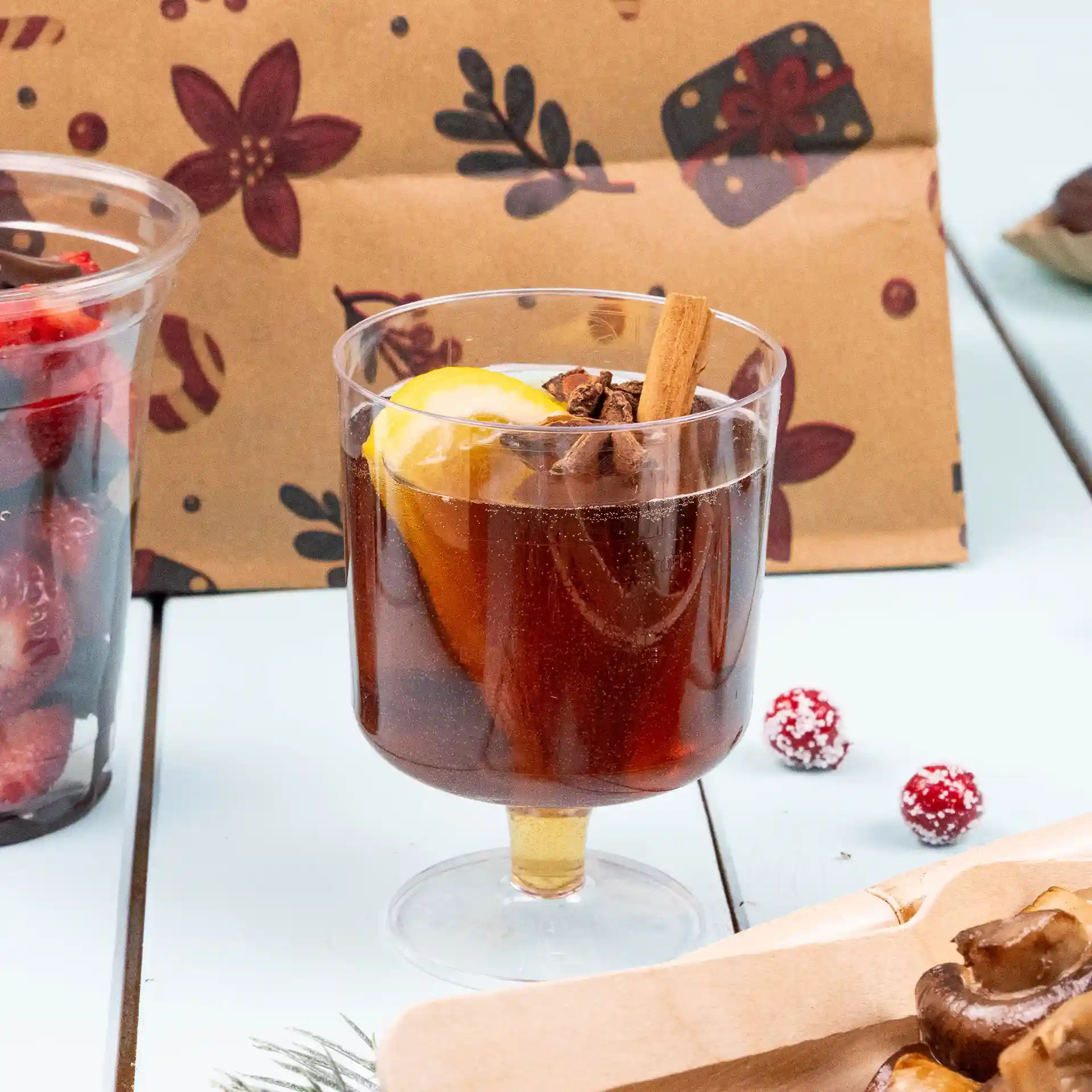 Transparent reusable wine glass filled with dark beverage, garnished with lemon slice and cinnamon stick.