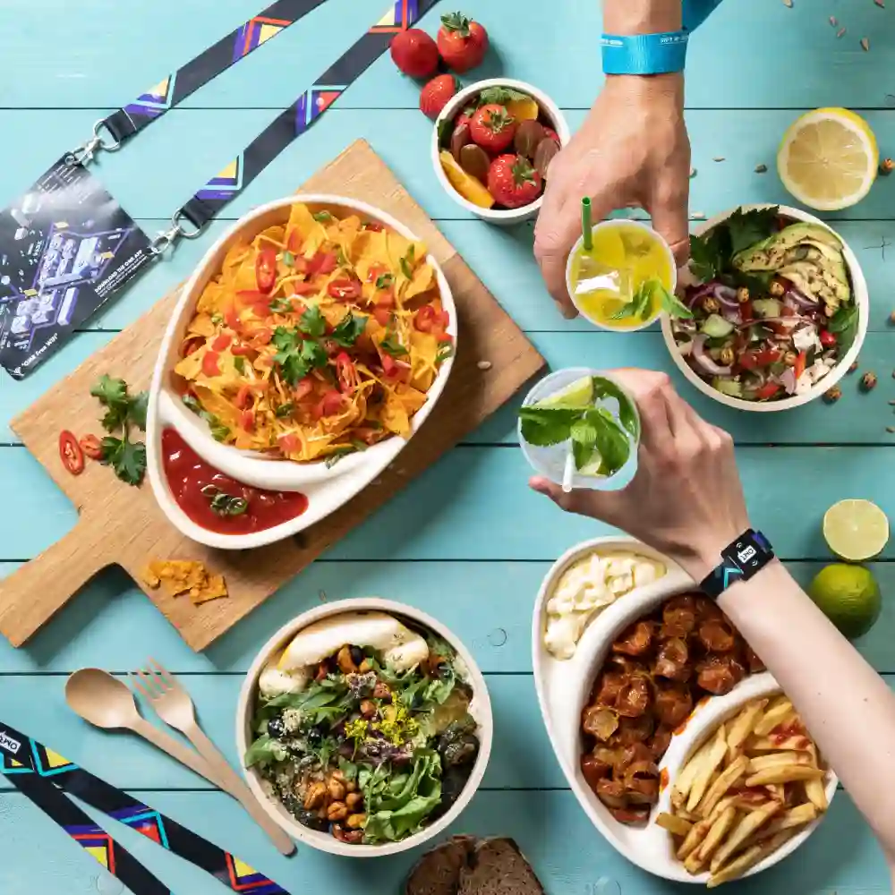 A top-down view of various food items including nachos, salads, and drinks on a blue surface with lanyards and utensils.