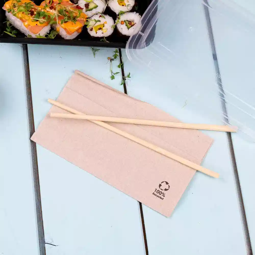 Brown paper napkins with wooden chopsticks placed on a blue table next to a sushi container.