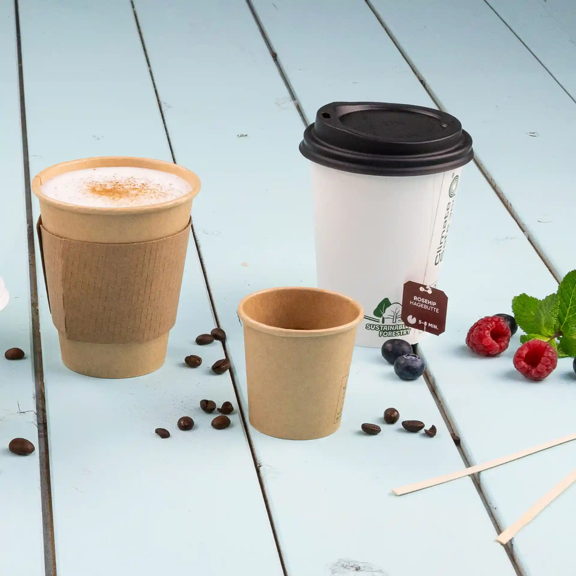 Image of three paper cups on a blue wooden surface, including a 300 ml white cup with a black lid, a brown cup, and a smaller brown cup.