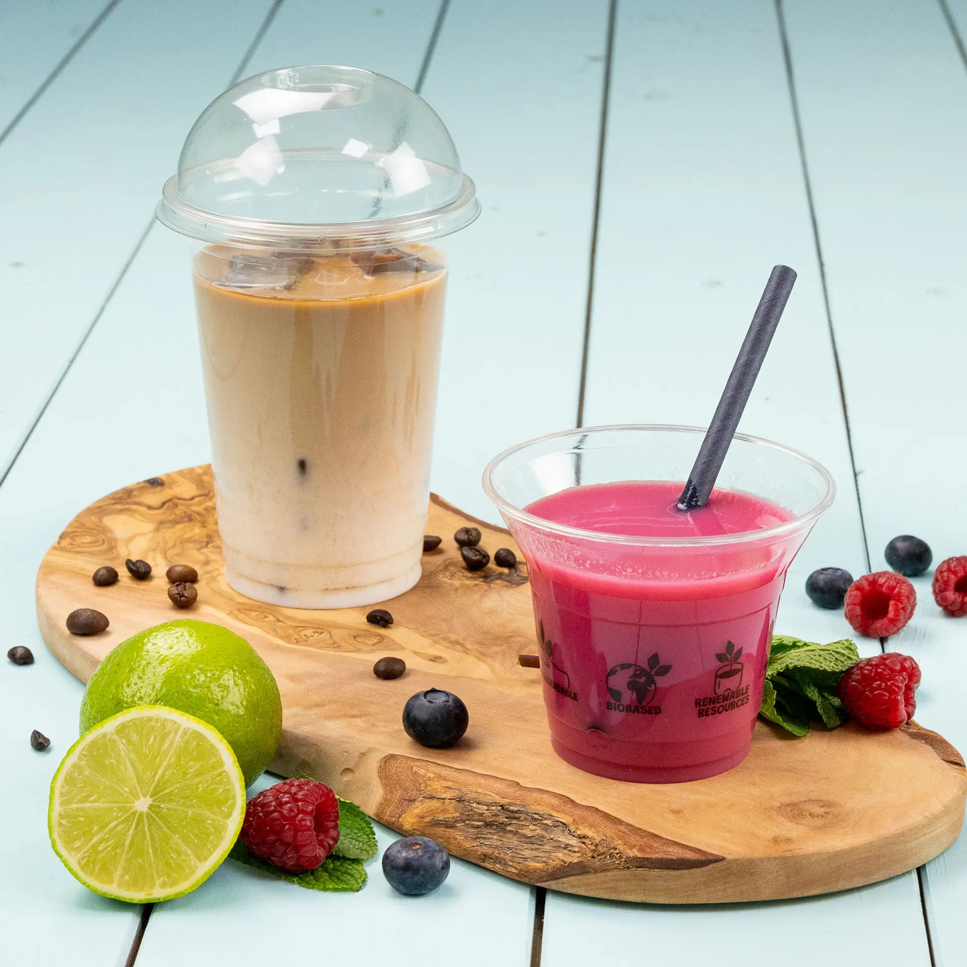 Transparent cups filled with cold beverages, including iced coffee and a pink drink, on a wooden serving board.