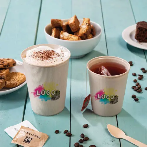 Two cups with logo design, one with whipped cream and the other with iced tea, surrounded by cookies, cake, and sugar packet.