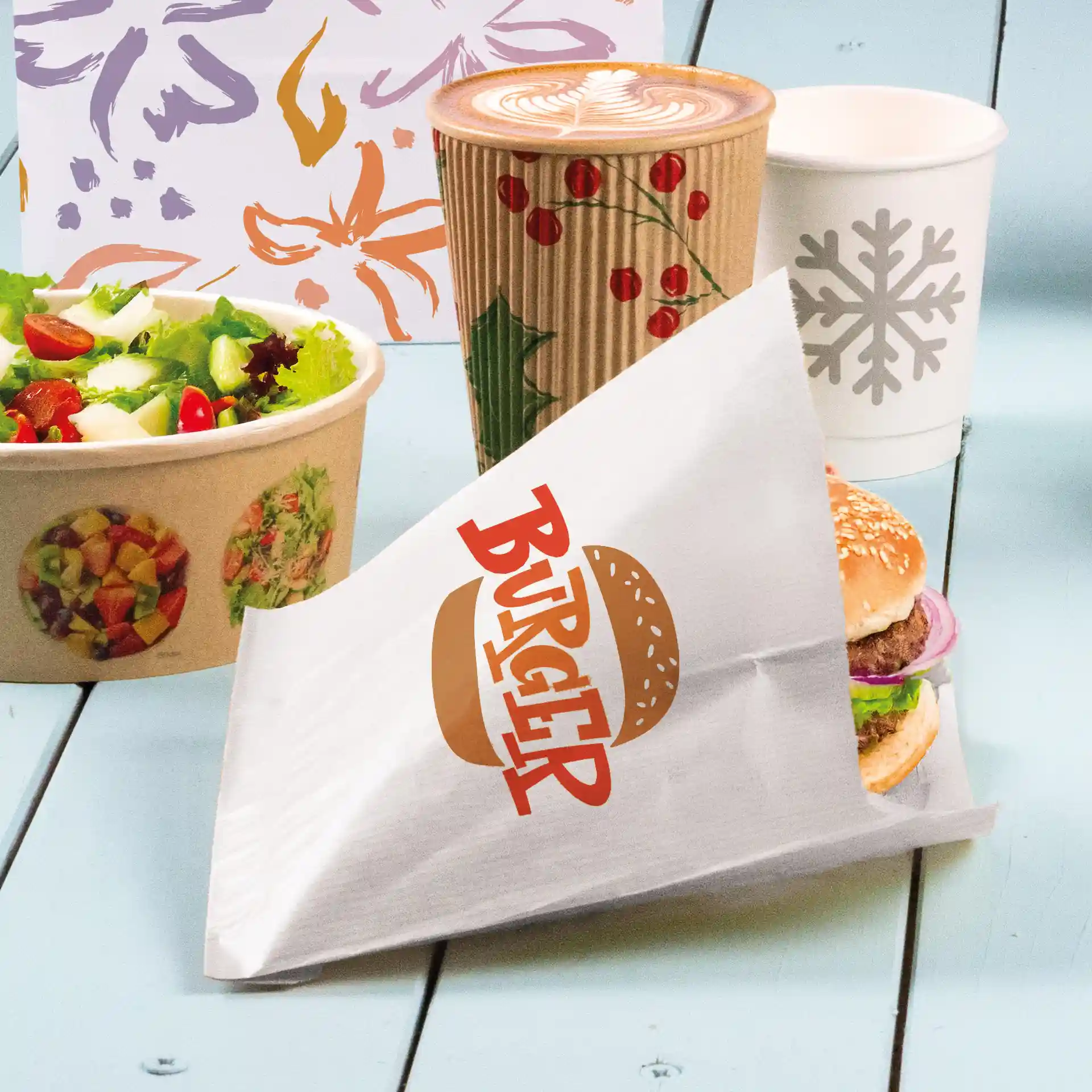 White burger sleeve with printed "BURGER" text, holding a burger with sesame seed bun, lettuce, and onion, alongside a salad and drinks.