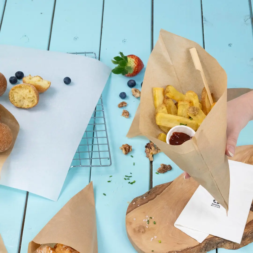 Brown paper cone filled with fries and a small cup of ketchup, surrounded by pastries, berries, and a wooden board.