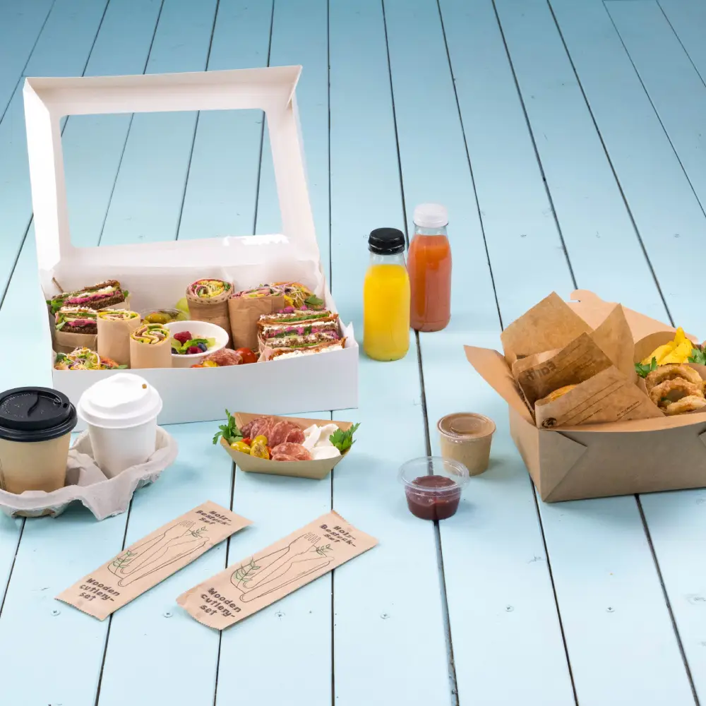 Catering event spread with assorted wraps in a box, beverages, a cup of coffee, and snacks on a blue wooden surface.