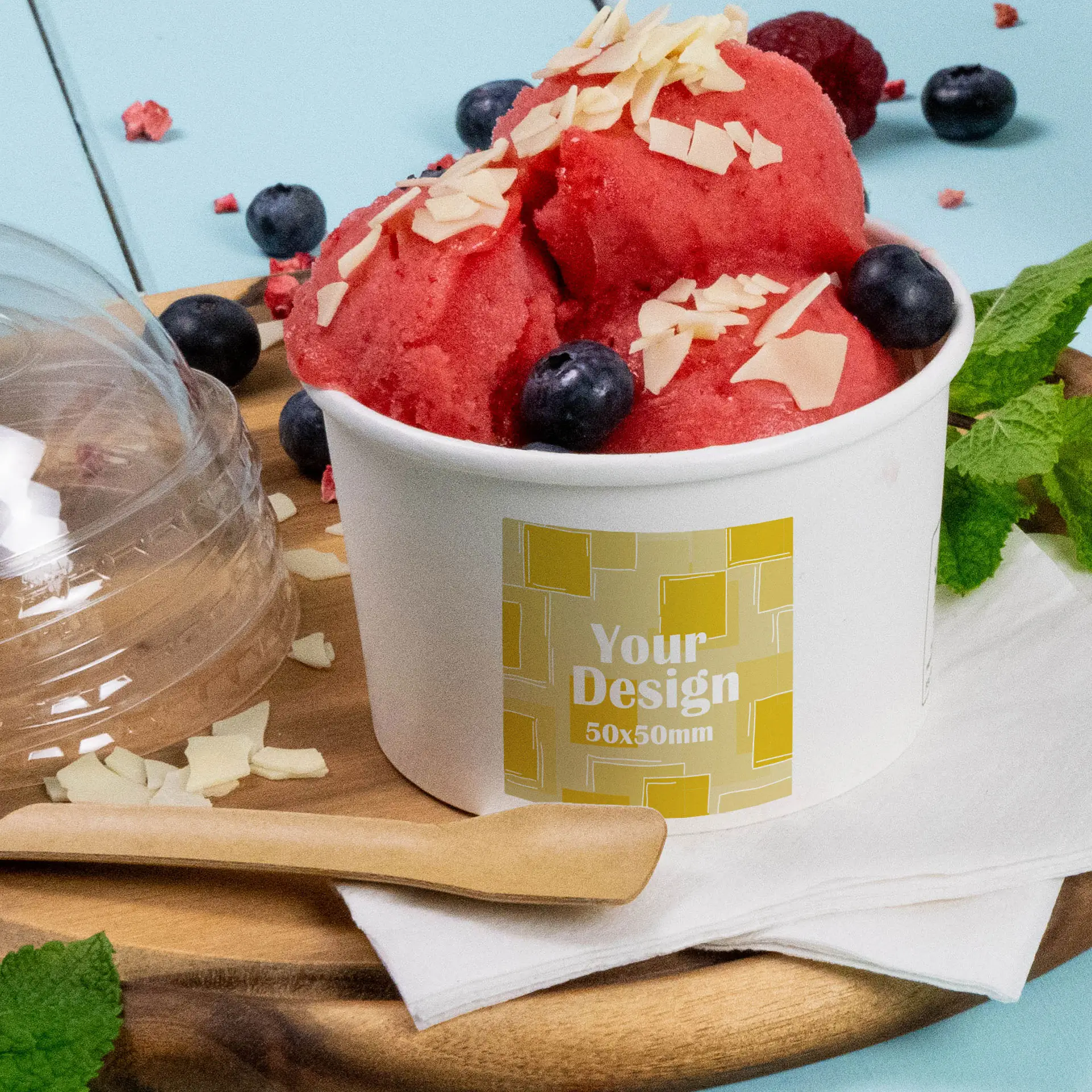 Cup of raspberry sorbet topped with sliced almonds and blueberries, on a wooden surface, with a custom printed label visible.