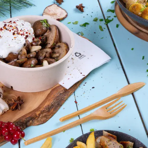 Bowl with sautéed mushrooms topped with yogurt and spices, accompanied by wooden utensils on a blue background.