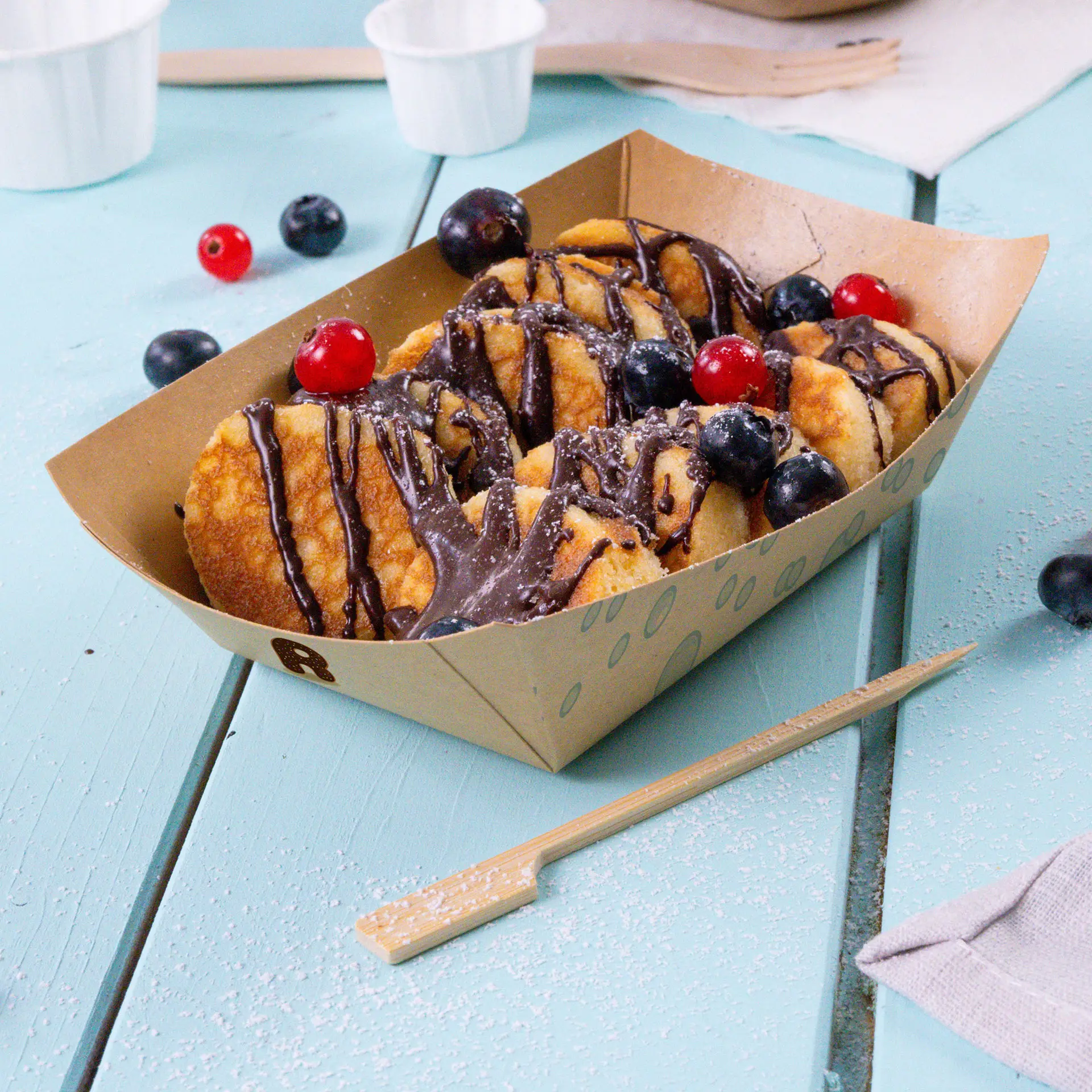 Brown custom-printed snack tray filled with fried snacks, drizzled with chocolate and topped with red cherries and blueberries.