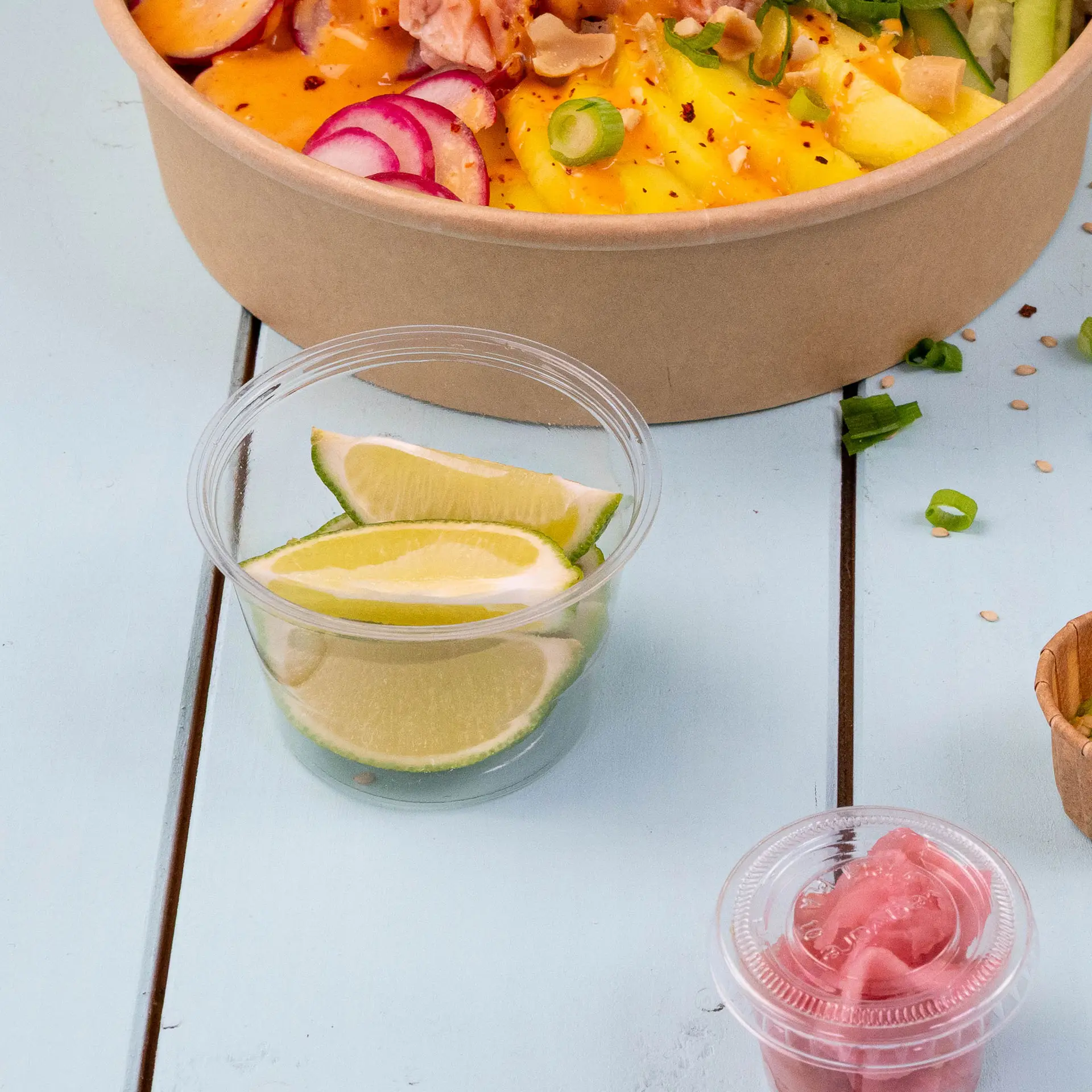 Clear PLA bio portion cups containing lime slices for dressing or dip, placed alongside a bowl of salad.