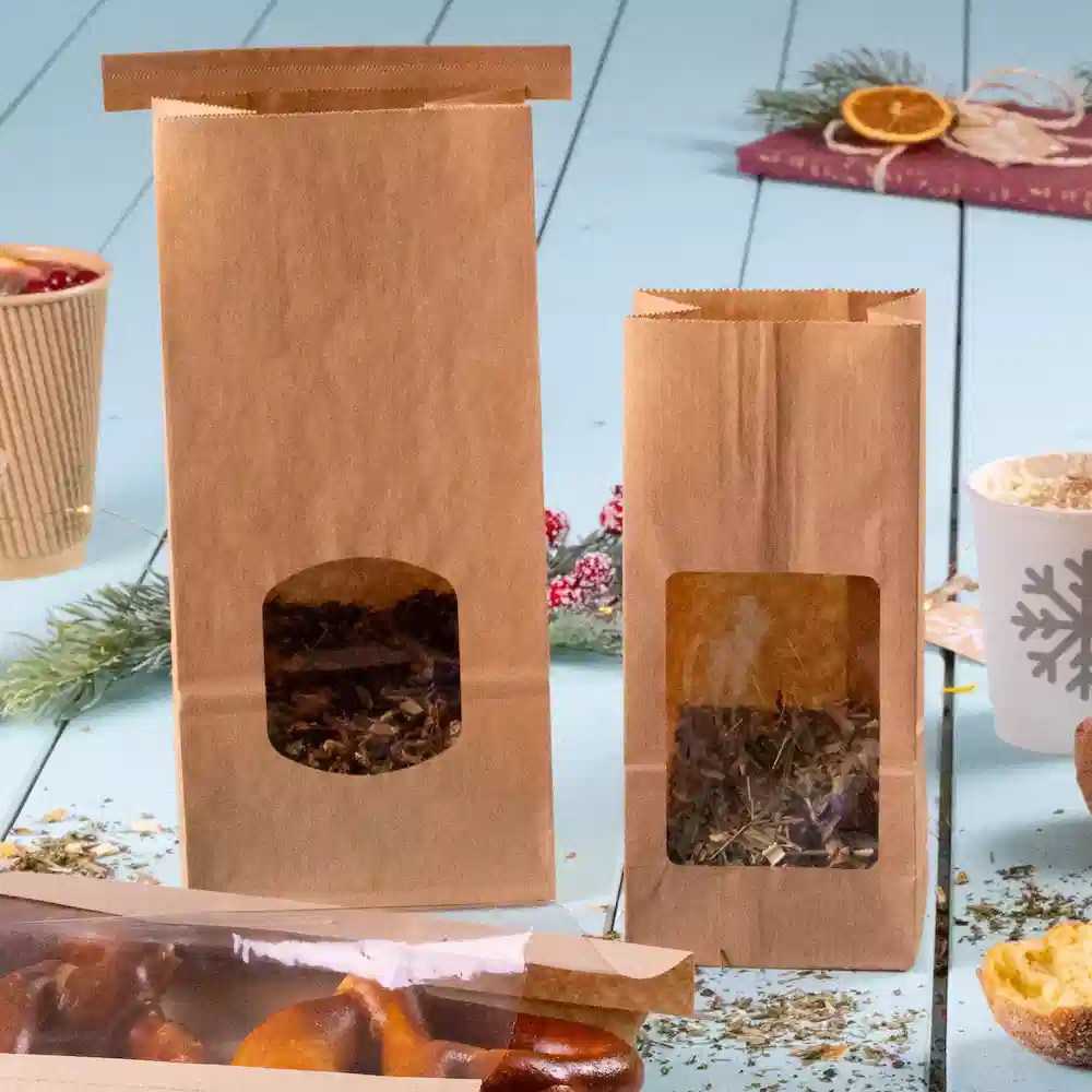 Two brown paper bags with transparent windows, one larger and one smaller, containing herbs or tea leaves.