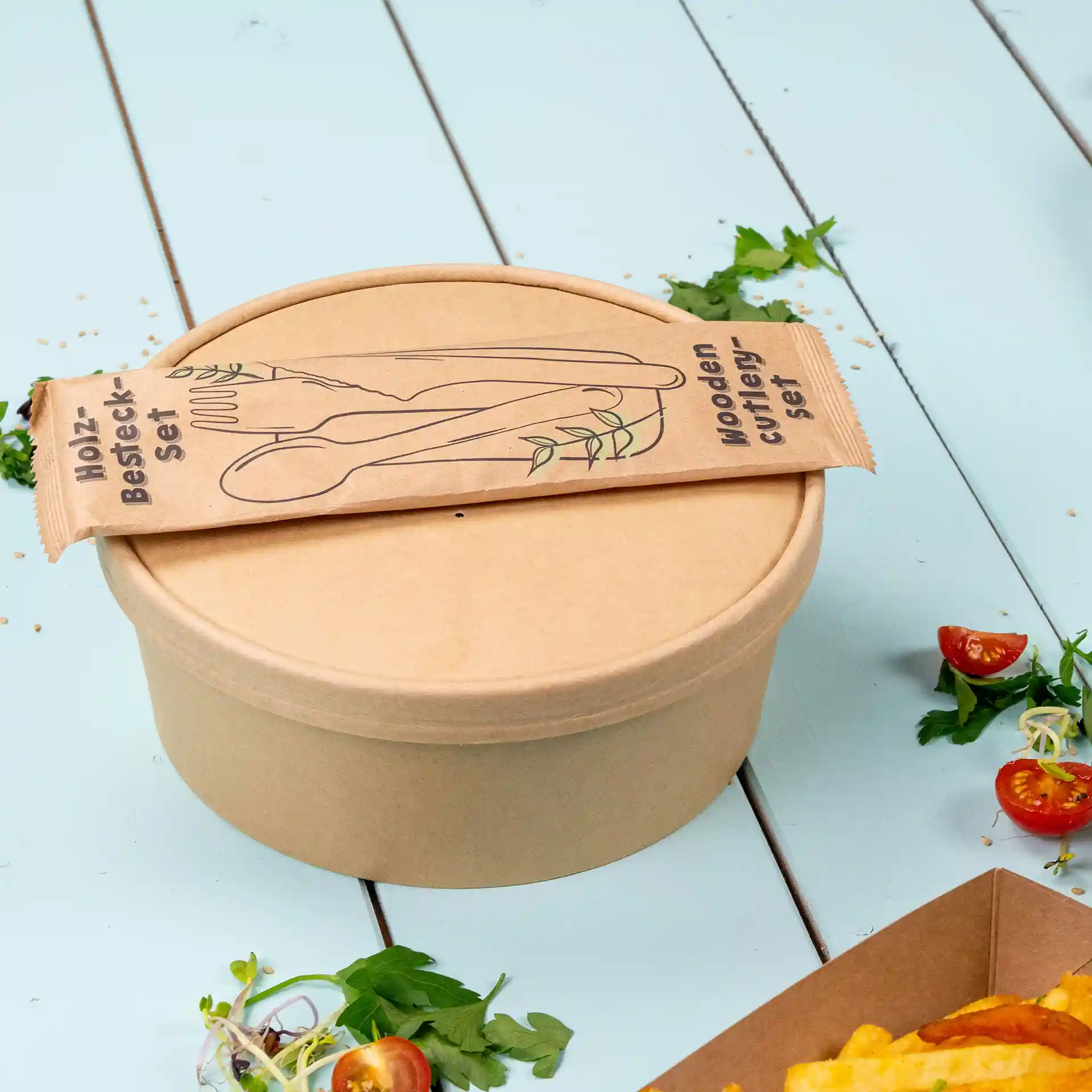 Brown round paper bowl with a lid, topped with a wooden cutlery set packaging.