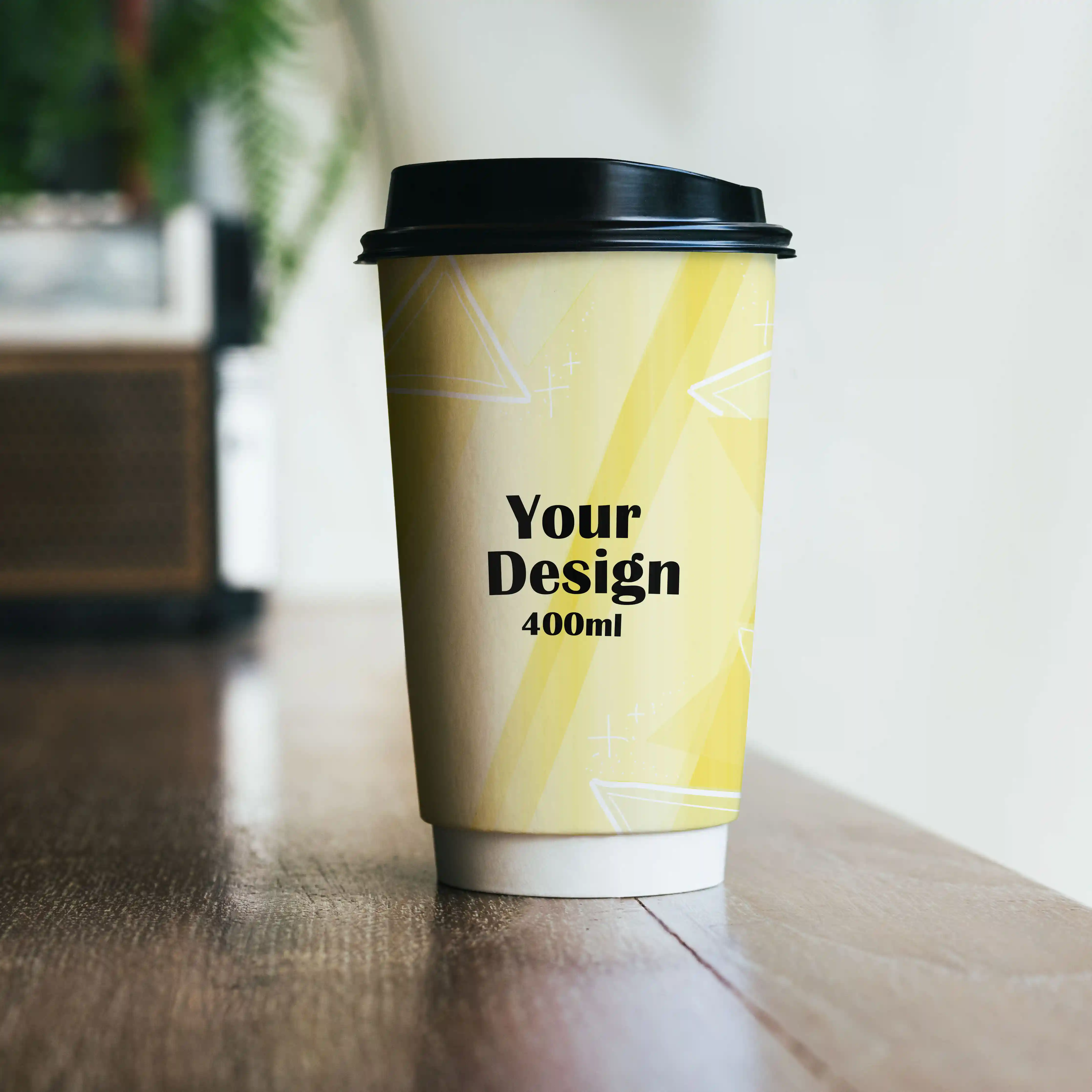 Double-walled paper cup with a yellow design, black lid, and a capacity of 400 ml, placed on a wooden surface.