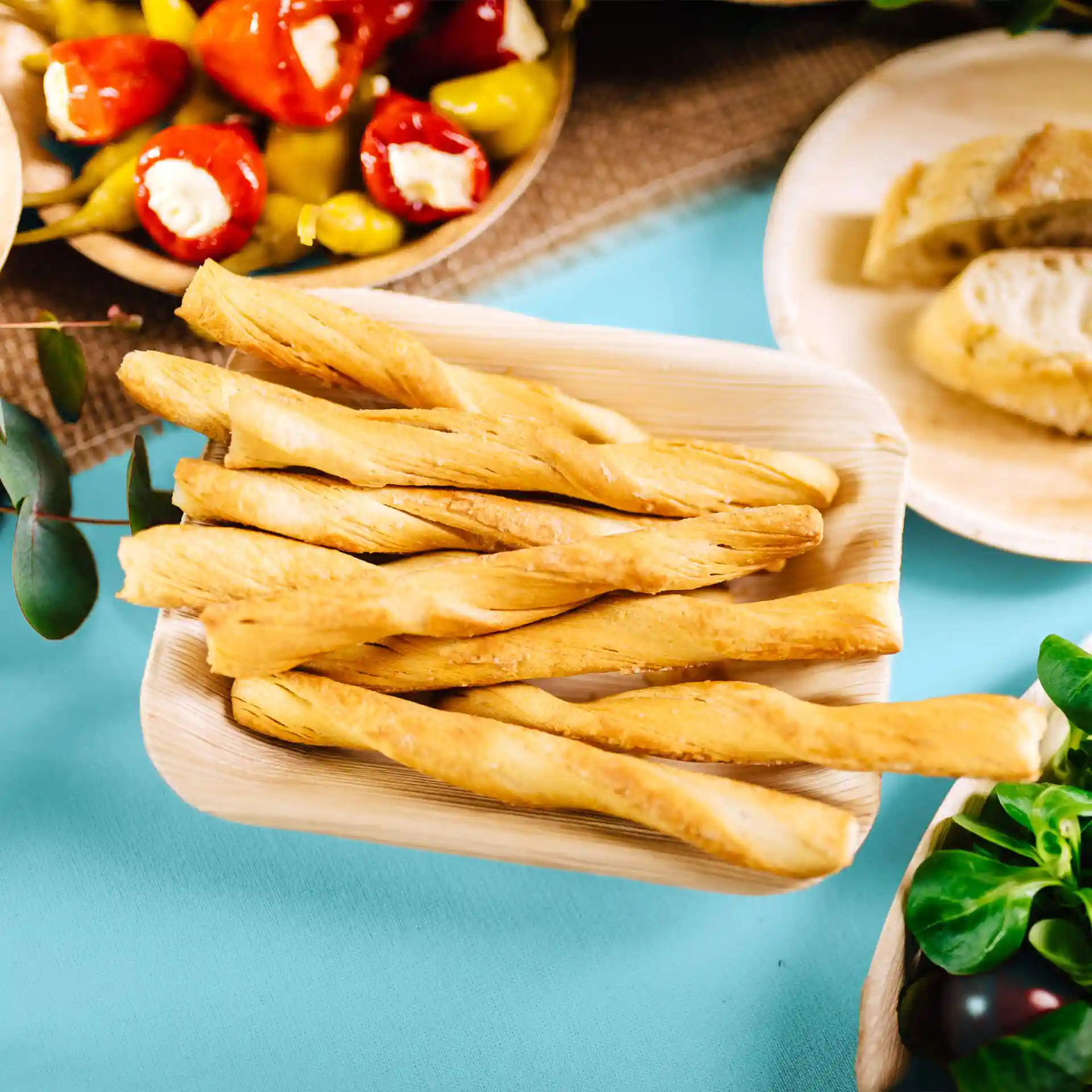 Deep rectangular palm leaf plate filled with twisted breadsticks on a blue background.