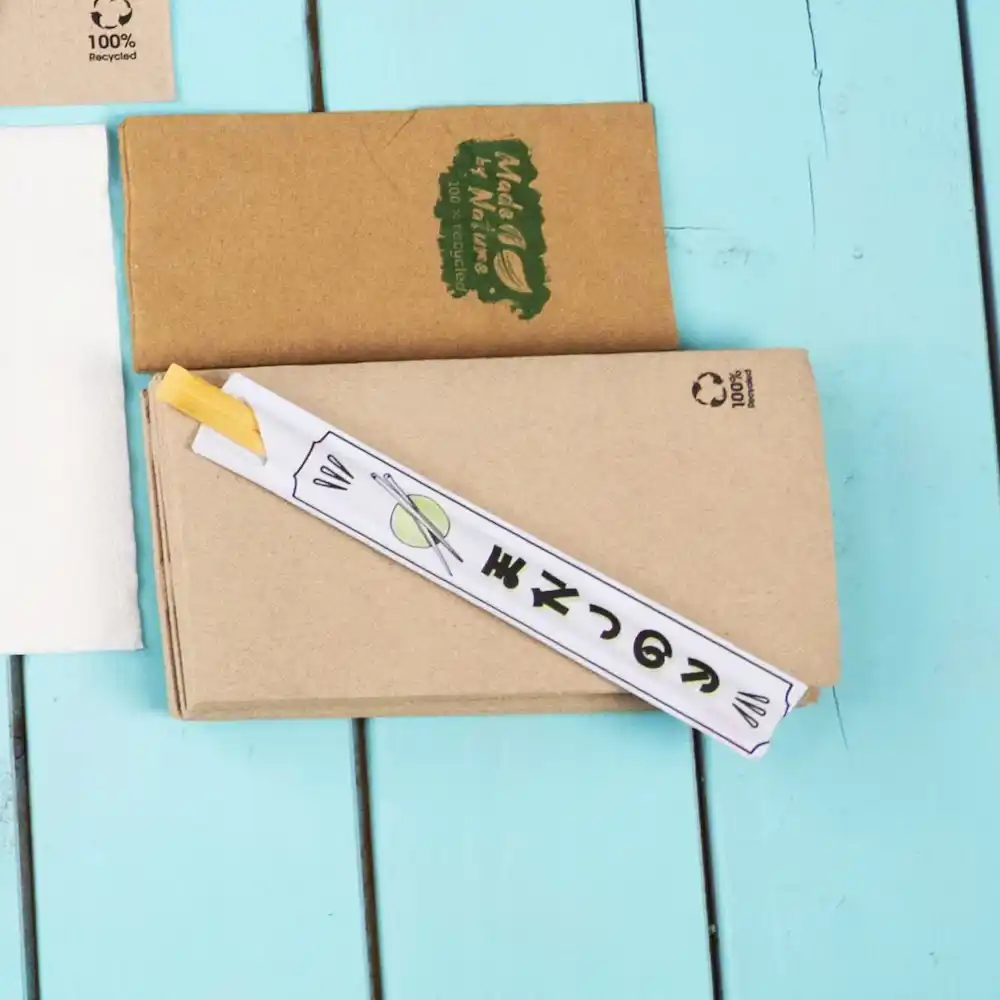 Chopsticks wrapped in paper on a blue wooden surface, with a brown kraft paper box in the background.