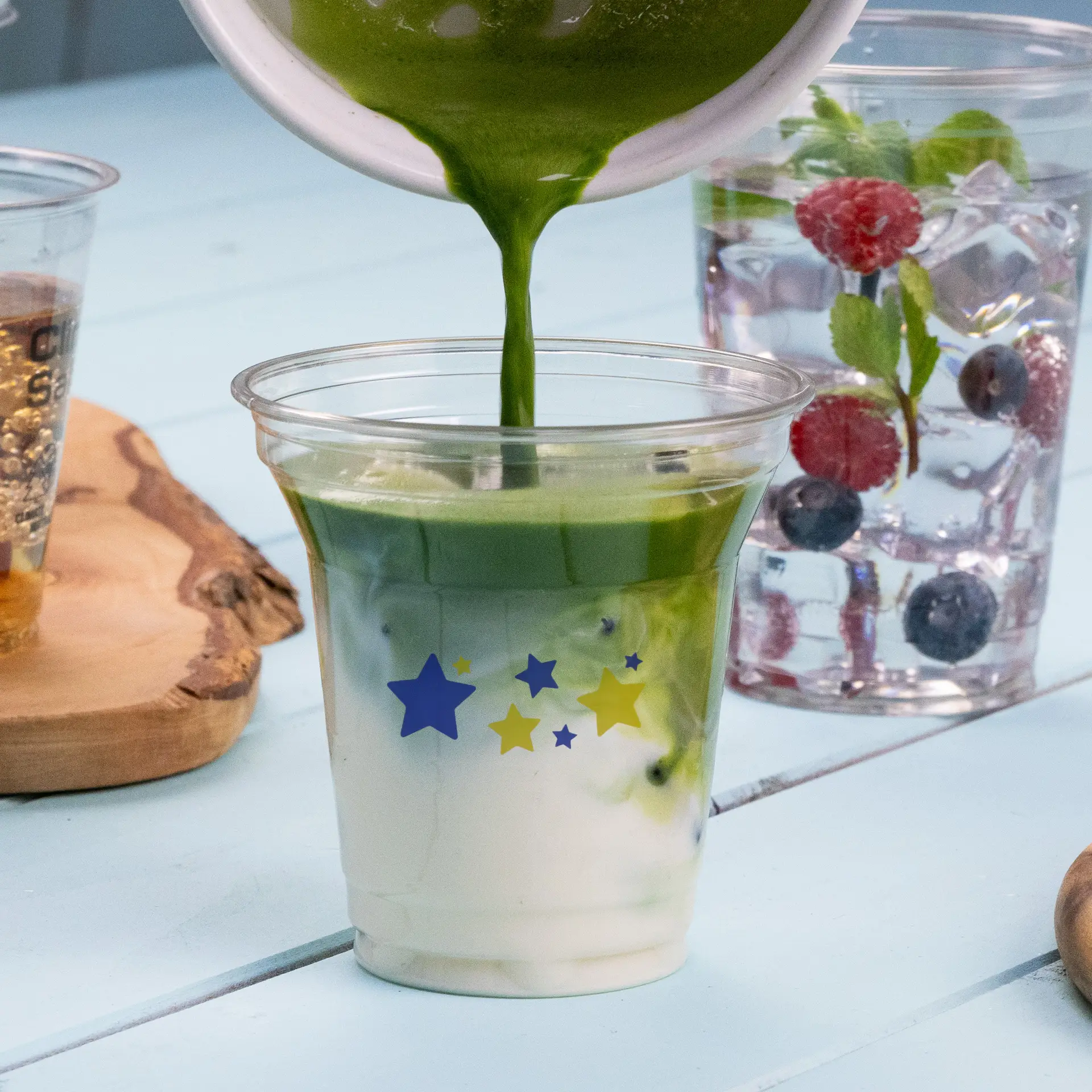 Pouring green beverage into an 8 oz rPET clear cup with star designs; other drinks displayed in background.