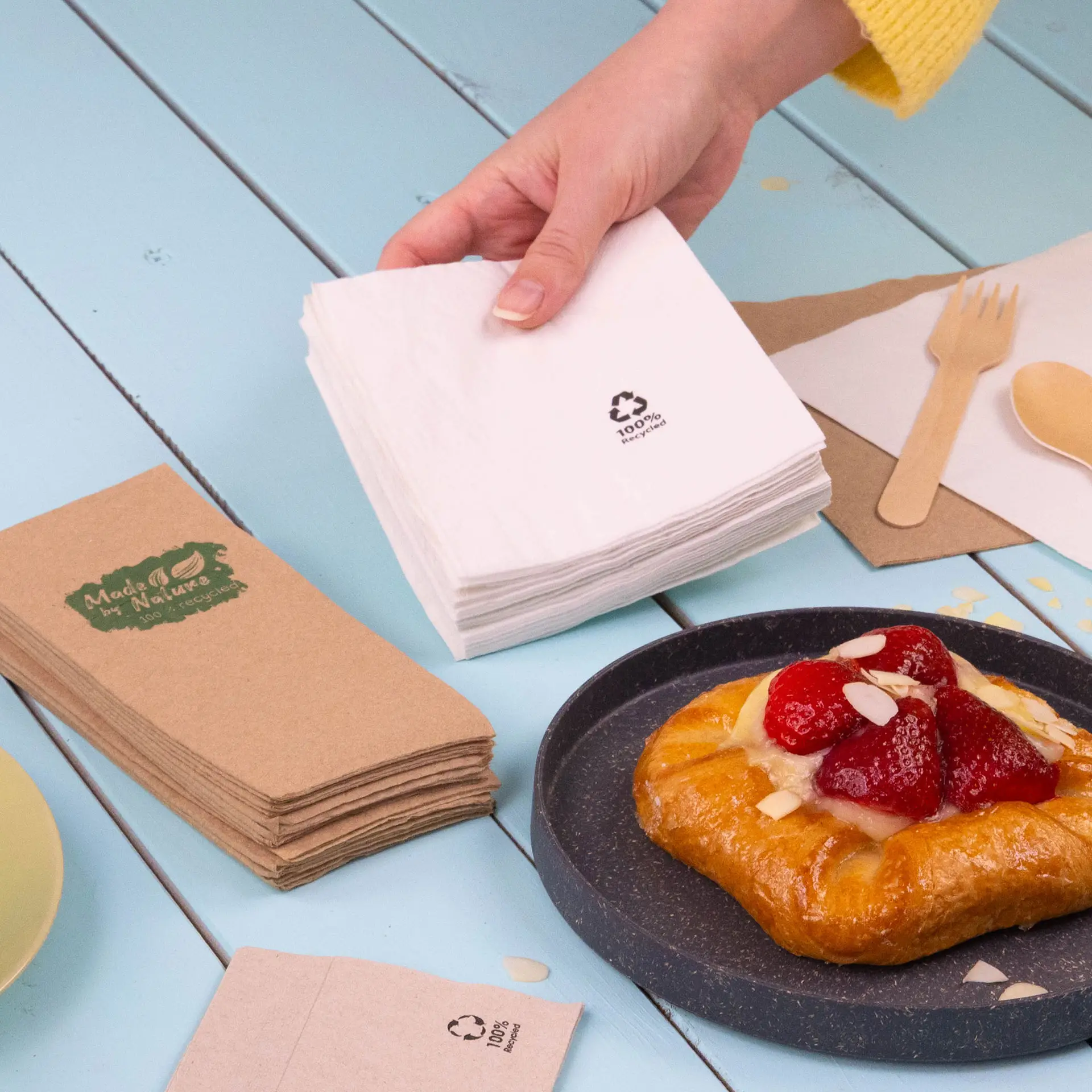 Two square cocktail napkins shown; one white and one light gray, both made from recycled paper, with recycling symbols.