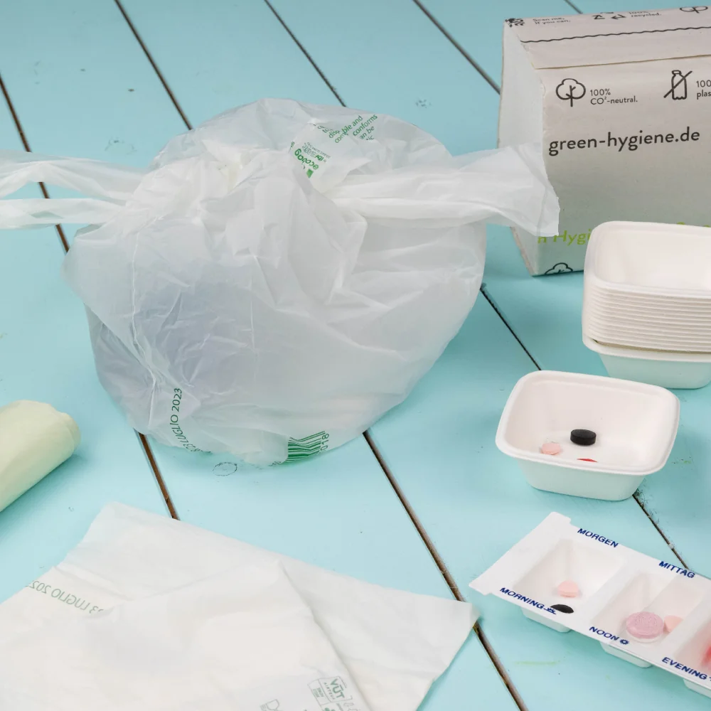 Plastic bag containing hygiene products; a white bowl with assorted items and a box labeled "green-hygiene.de" nearby.