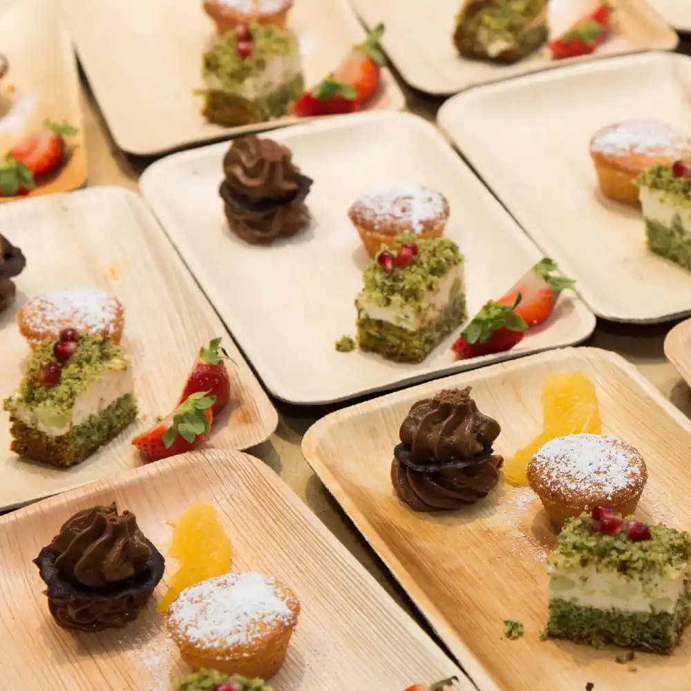 Assorted desserts on biodegradable trays, featuring layered cake, cupcakes with frosting, and strawberries.