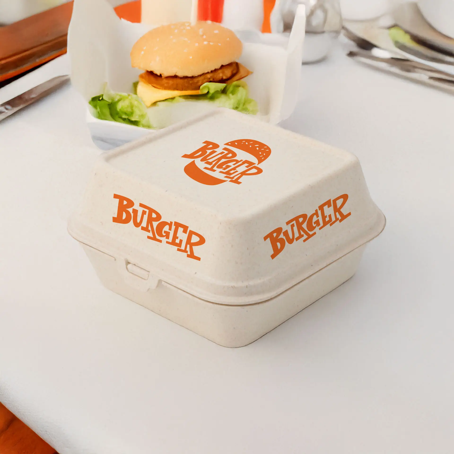 Cream white reusable burger box with orange "BURGER" logo, suitable for hot and cold foods, next to a hamburger on a table.