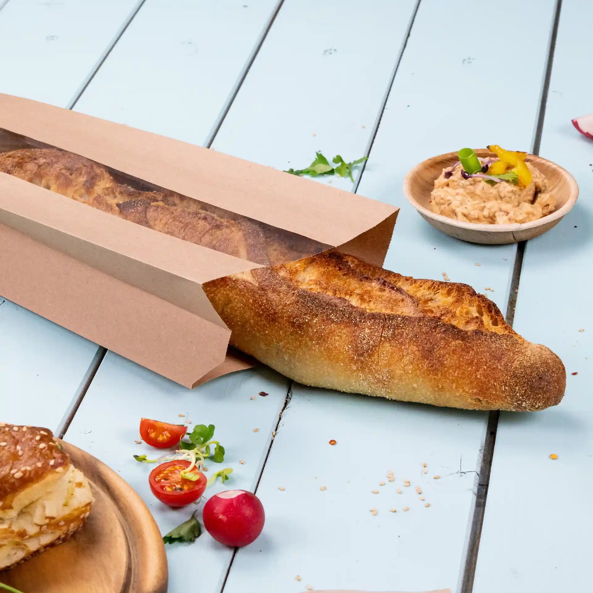 Brown flat paper bread bag with a window, containing a baguette, placed on a light blue wooden surface.