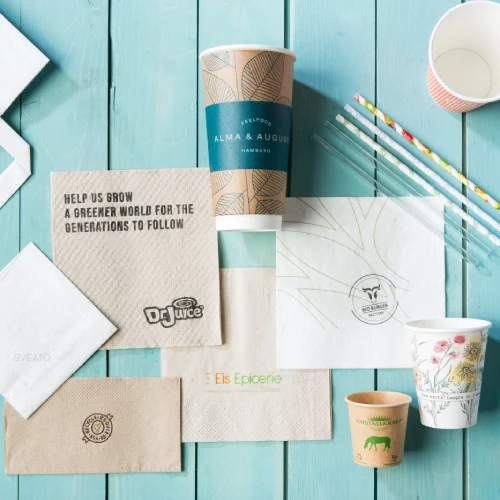 Brown and white paper napkins, disposable cups, and straws displayed on a blue wooden surface.