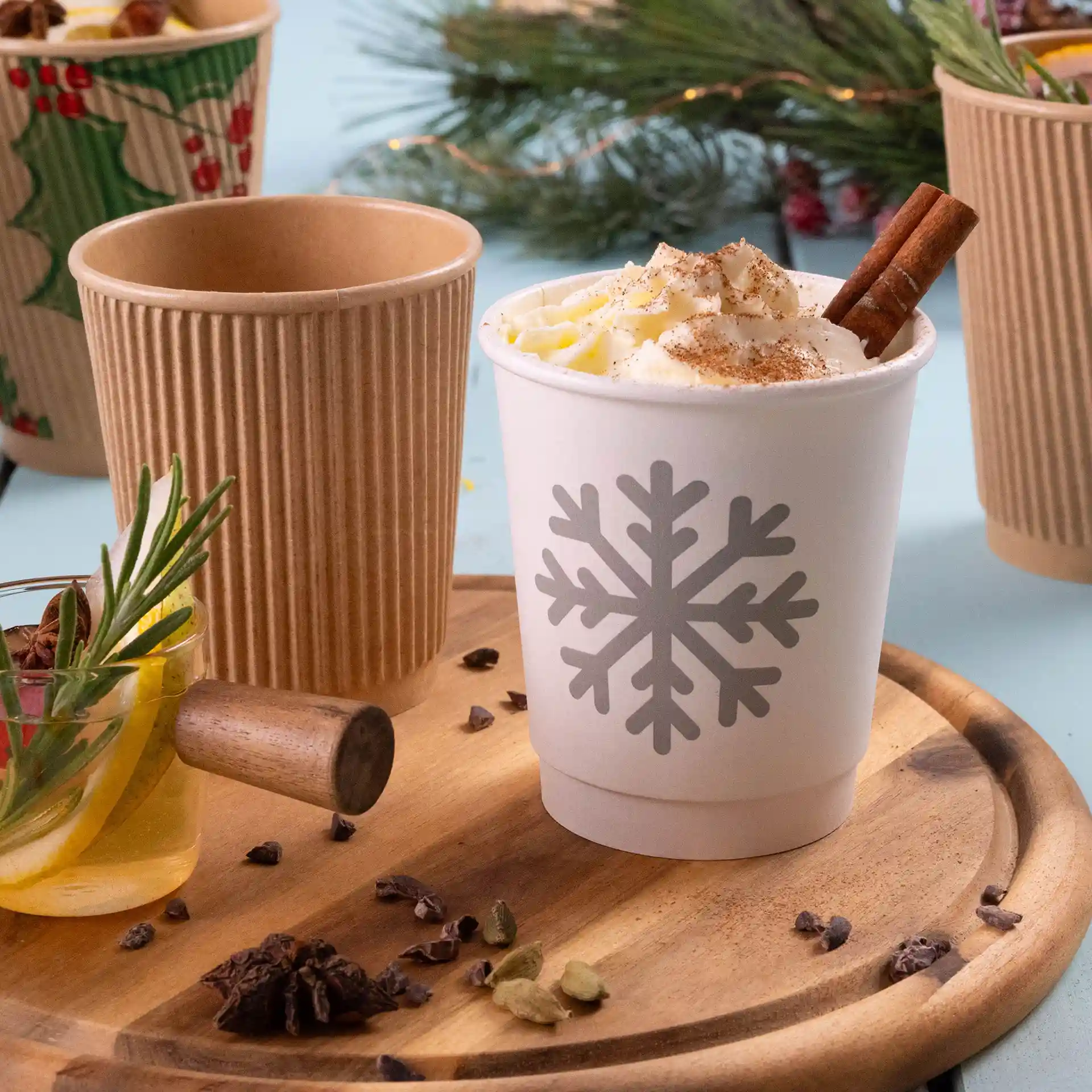 White paper cup with a snowflake design, filled with whipped cream and a cinnamon stick, on a wooden tray.