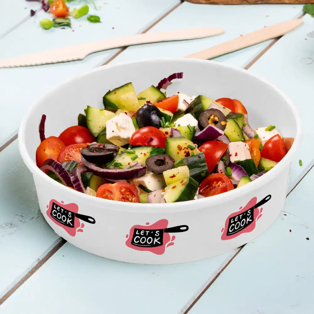White bowl filled with fresh salad containing tomatoes, cucumbers, olives, and feta cheese, labeled with "LET'S COOK."