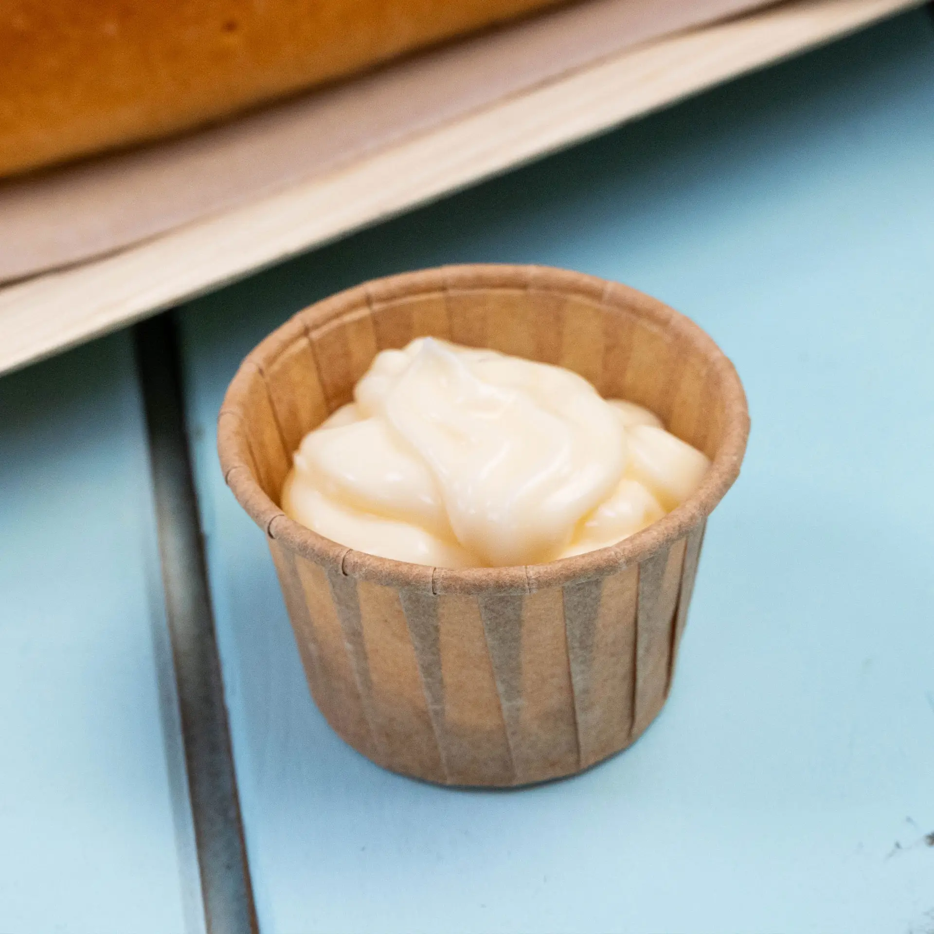Small brown paper cup containing a creamy dip, ideal for sauces and tasting portions, set on a blue surface.