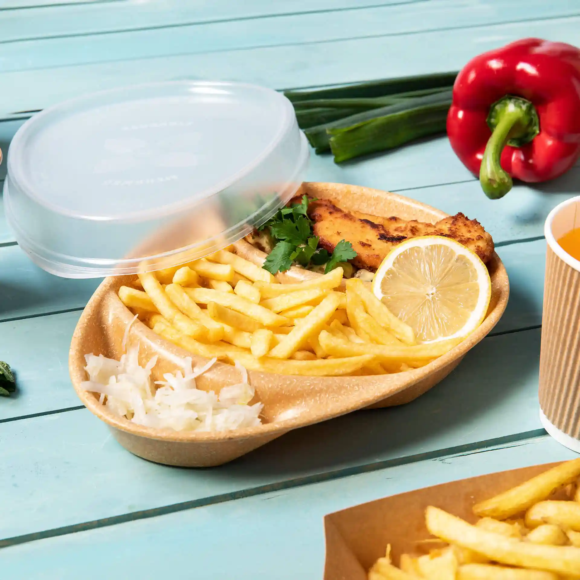 Brown reusable plate with three compartments, containing fries, fish, lemon, and garnish, with a clear lid on top.