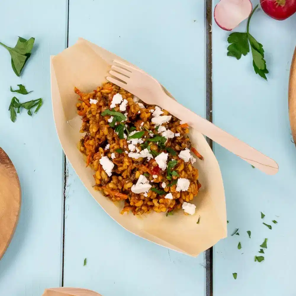 Wooden fork on a dish of seasoned rice with herbs and crumbled cheese on a blue tabletop.