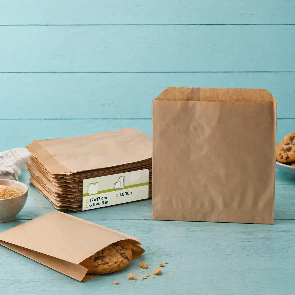 Brown paper bags stacked next to an open bag with a cookie inside, on a blue wooden background.