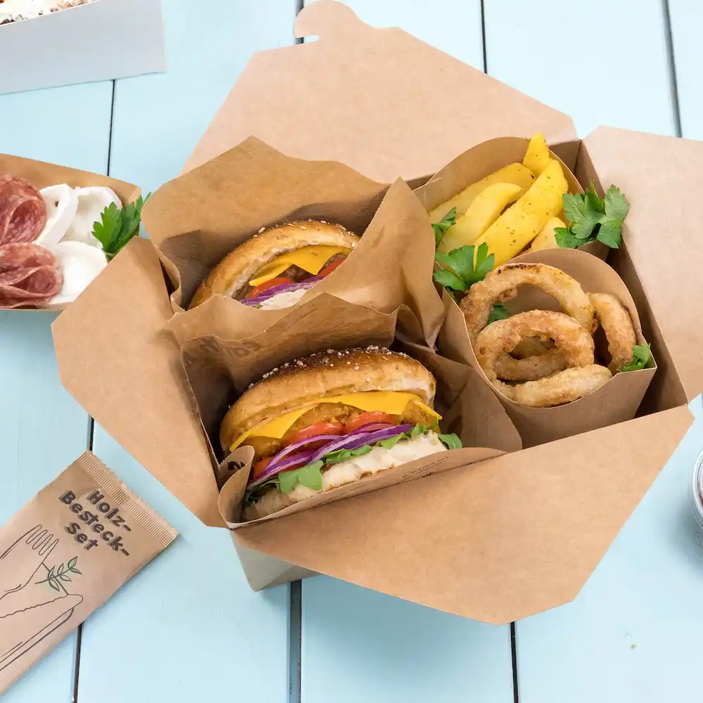 Two hamburgers with cheese, lettuce, tomato, and onion in a takeout box, accompanied by onion rings and fries.