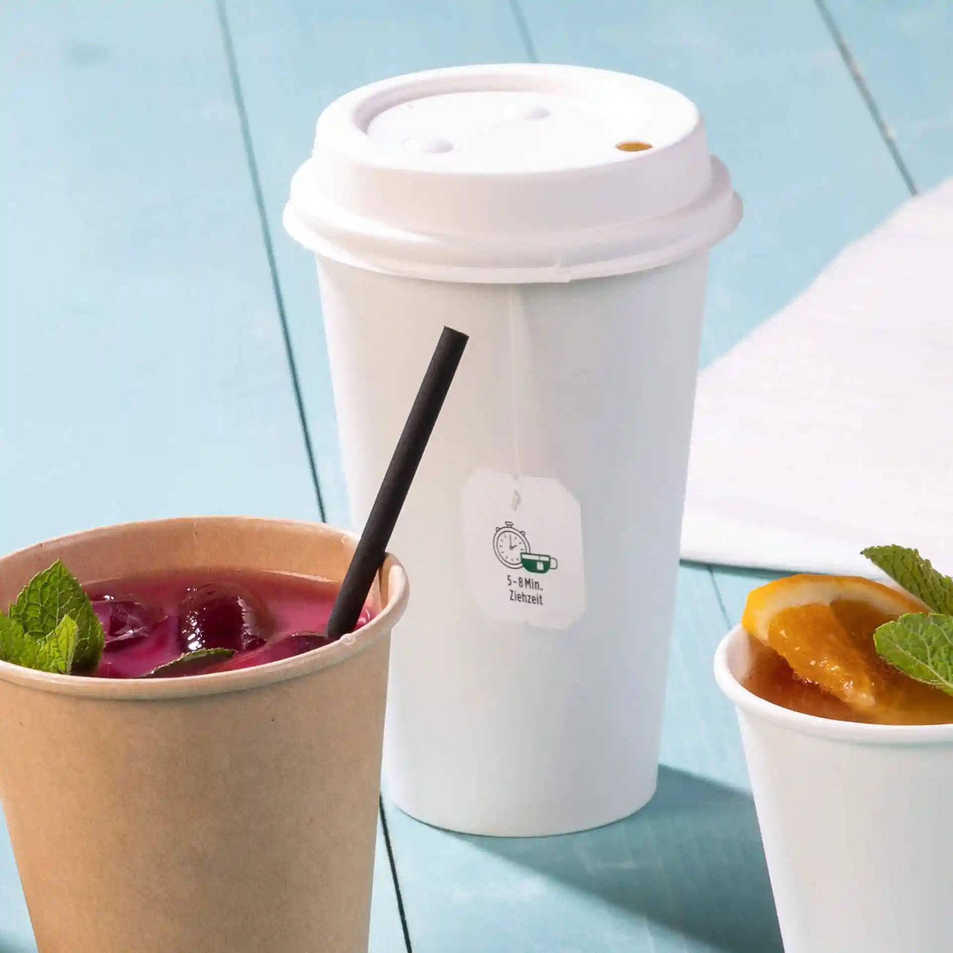 White paper cup with a lid, 500 ml capacity, next to a brown cup with a black straw and a white cup with fruit.
