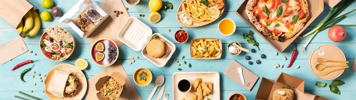 A variety of food items arranged on a blue surface, including pizza, salads, burgers, and desserts in containers.