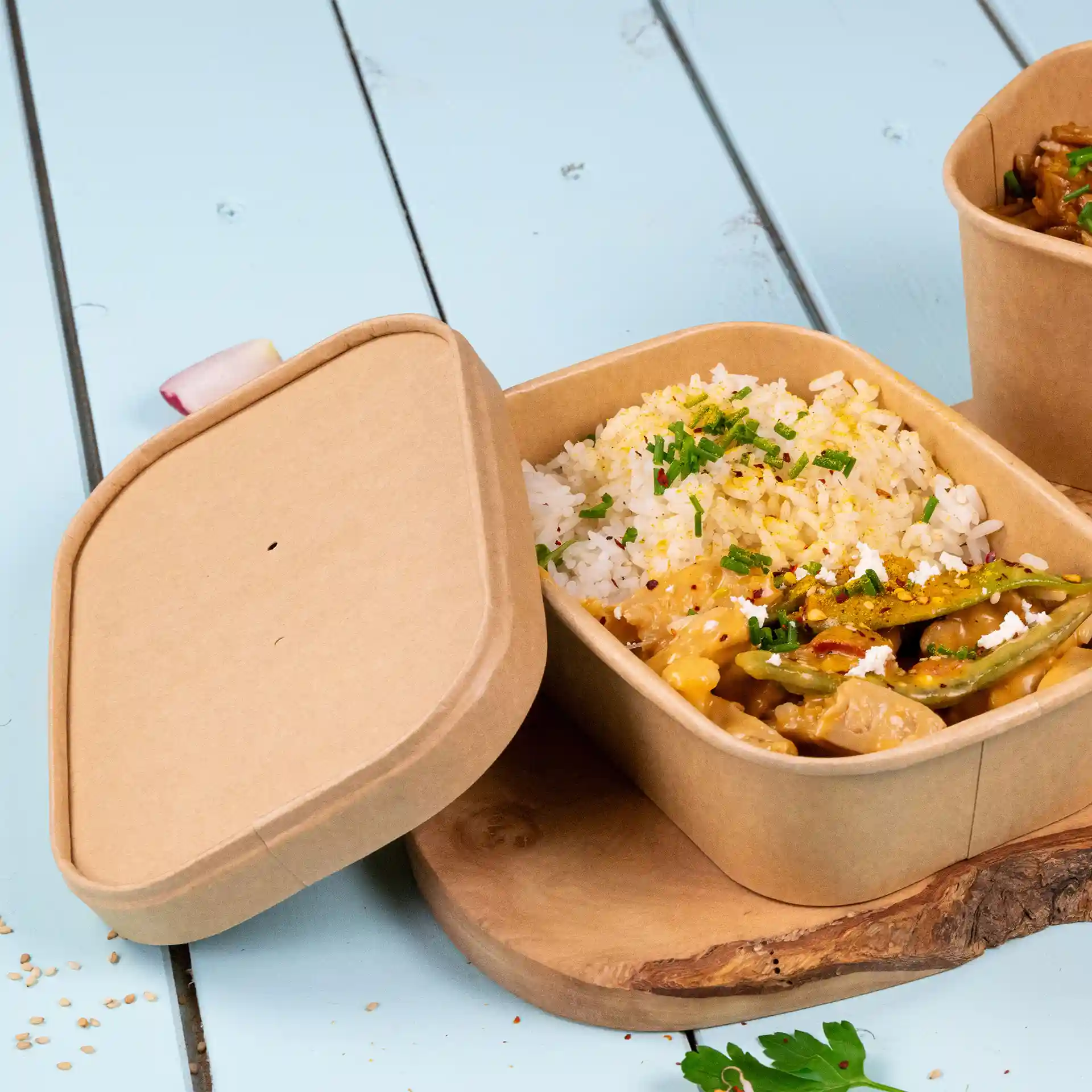 Brown rectangular cardboard container with rice and vegetables, partially open on a wooden surface.