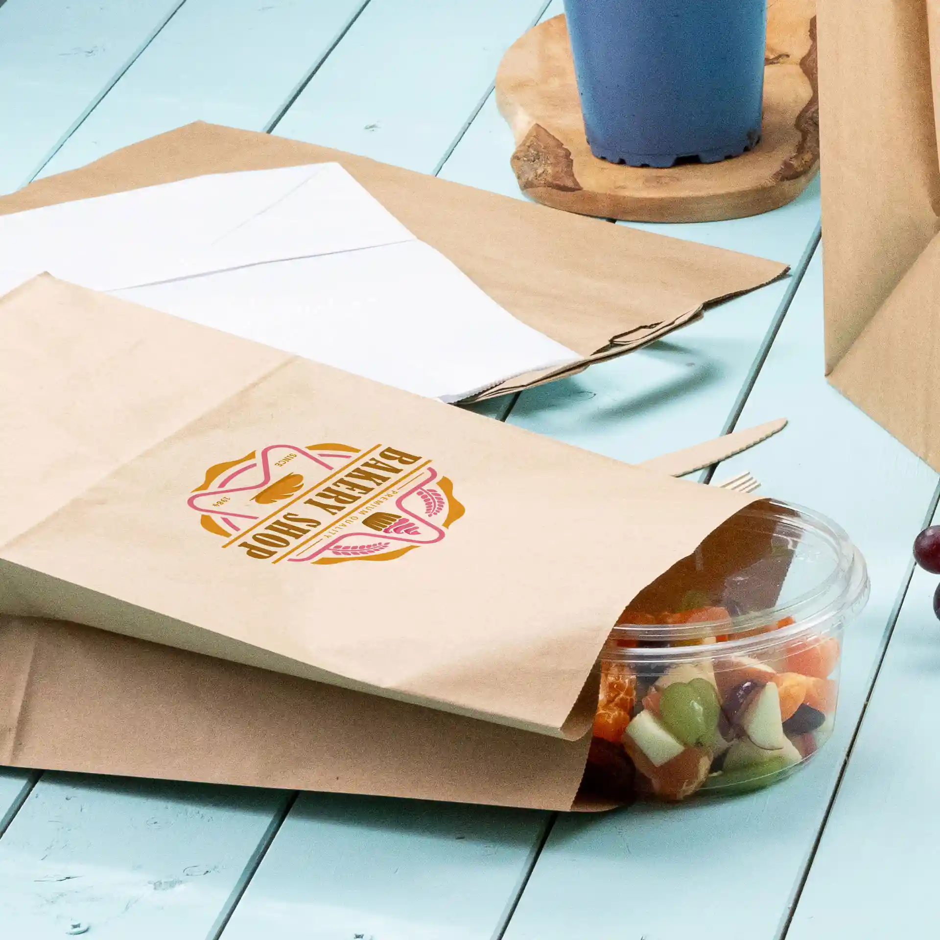 Brown printed paper bag with a circular green design, partially open with a clear container of mixed fruit beside it.