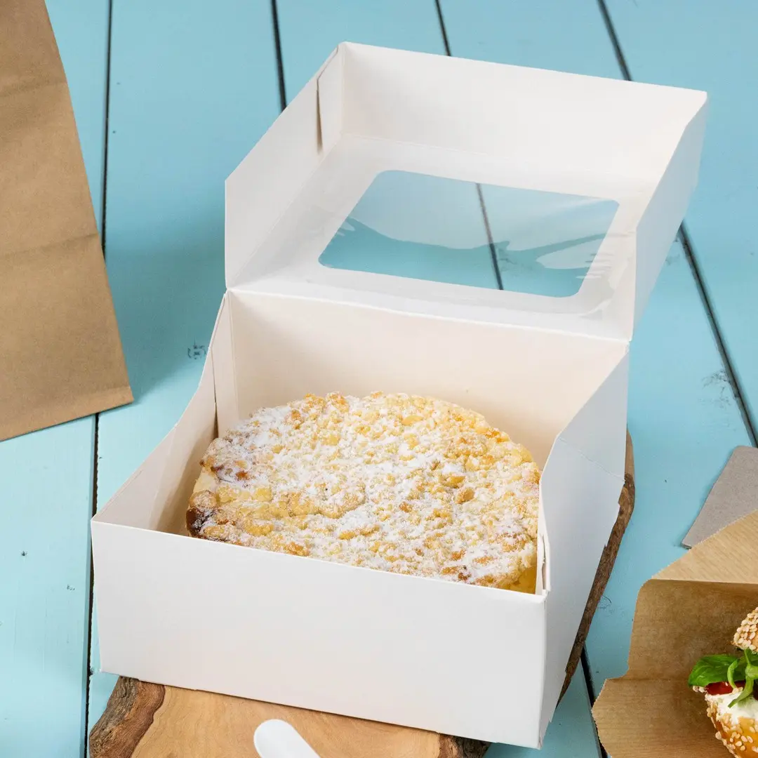 White cake box with a clear window, containing a round cake dusted with powdered sugar, on a wooden surface.