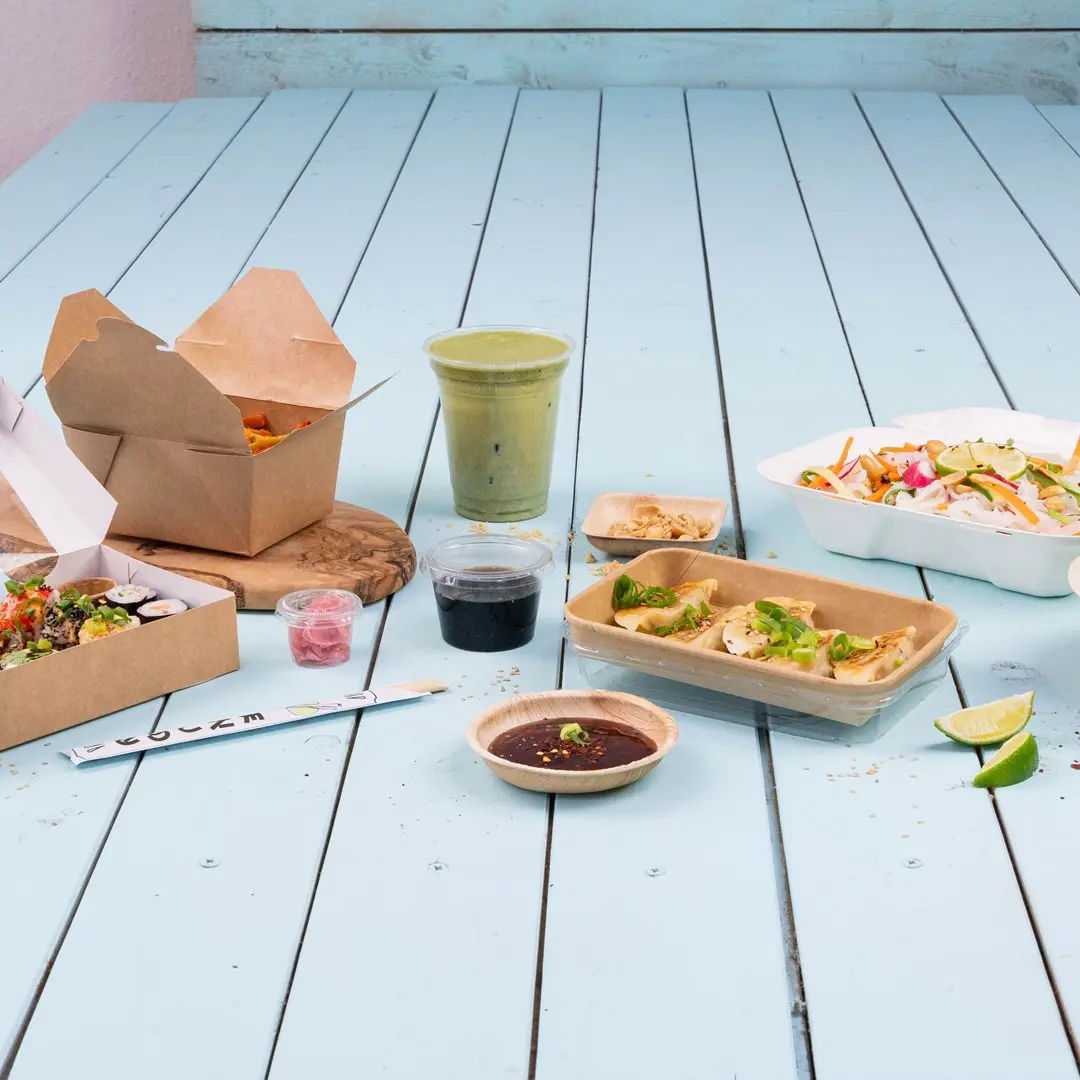 Assorted Asian food items on a blue wooden table, including sushi, dumplings, salad, and a green drink.