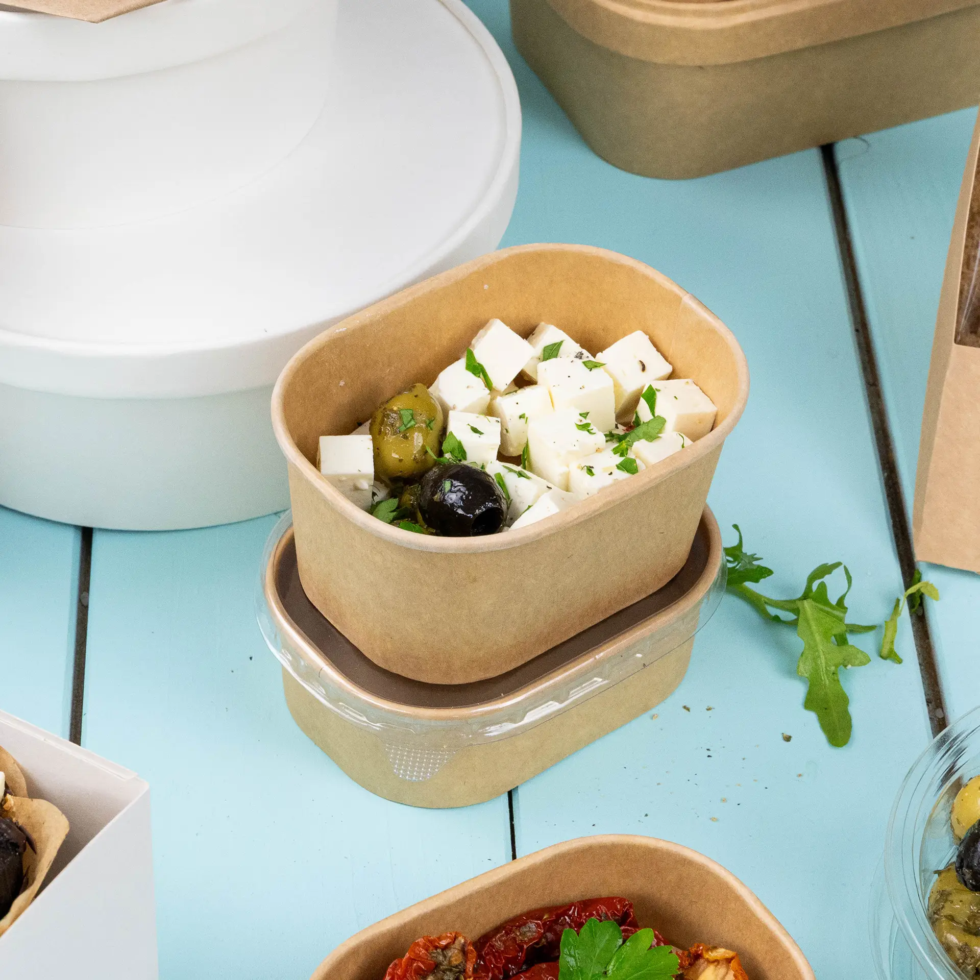 One kraft food container filled with feta cheese cubes and olives, with another similar container below it.