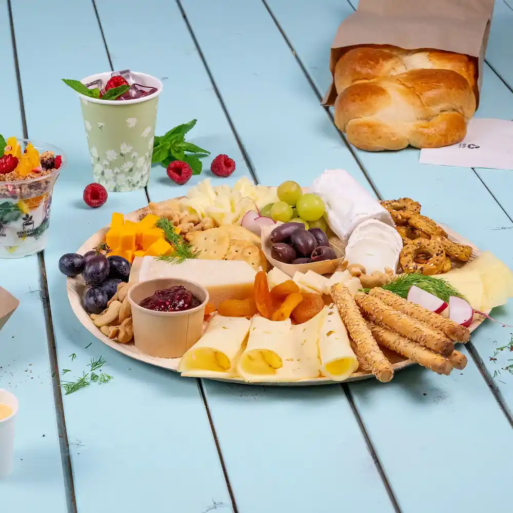 Platter with assorted cheeses, crackers, fruits, nuts, and bread on a blue wooden surface.