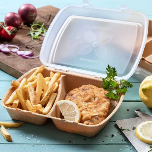 Container with fried chicken, lemon wedge, and French fries, surrounded by food items and a cutting board.
