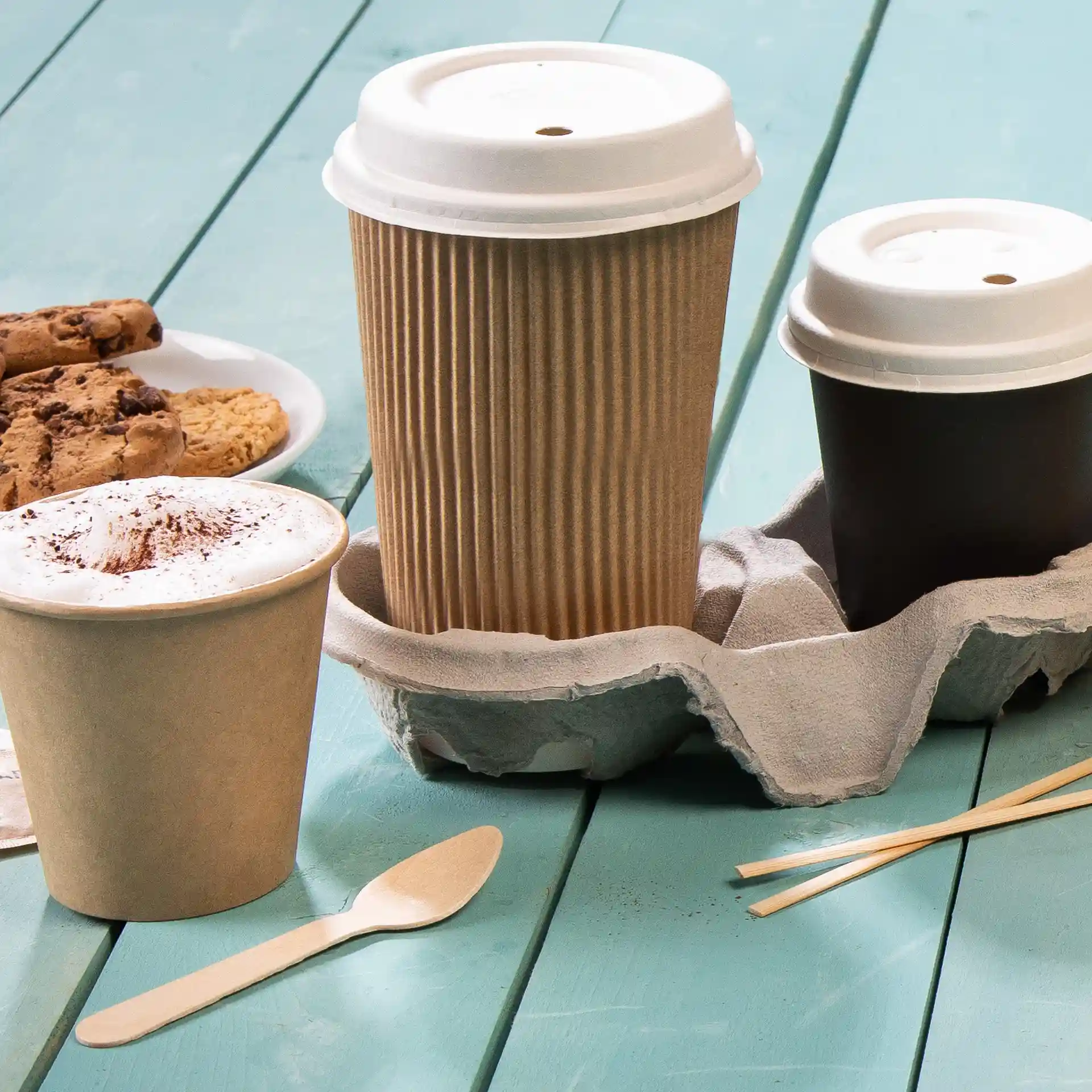 Image of three coffee cups in a cardboard holder on a blue wooden surface, with cookies on a plate nearby.