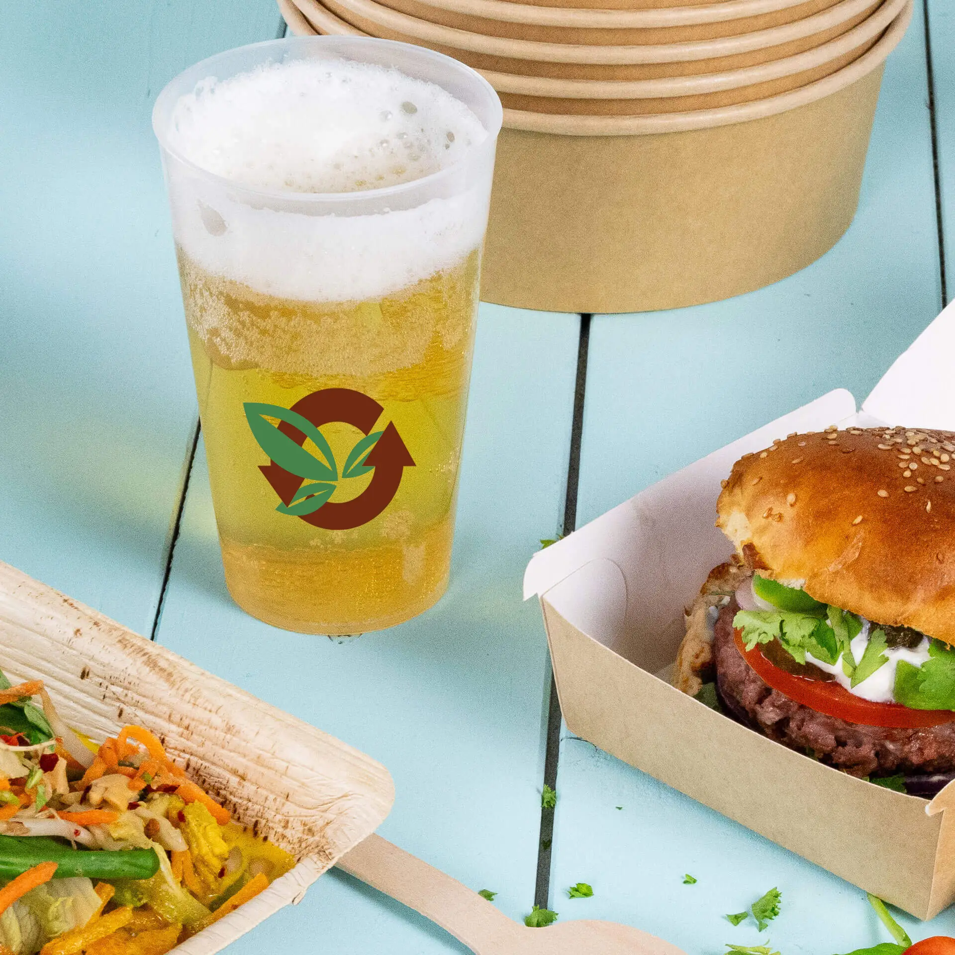 Reusable 400 ml cup with logo and foam beer, alongside a burger and salad on a blue wooden table.