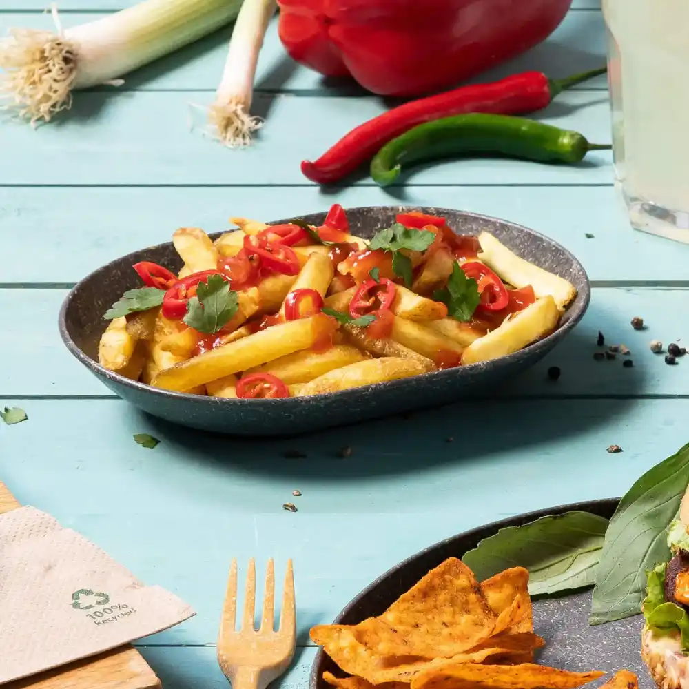 Bowl of French fries topped with sliced chili peppers and cilantro on a blue wooden table.